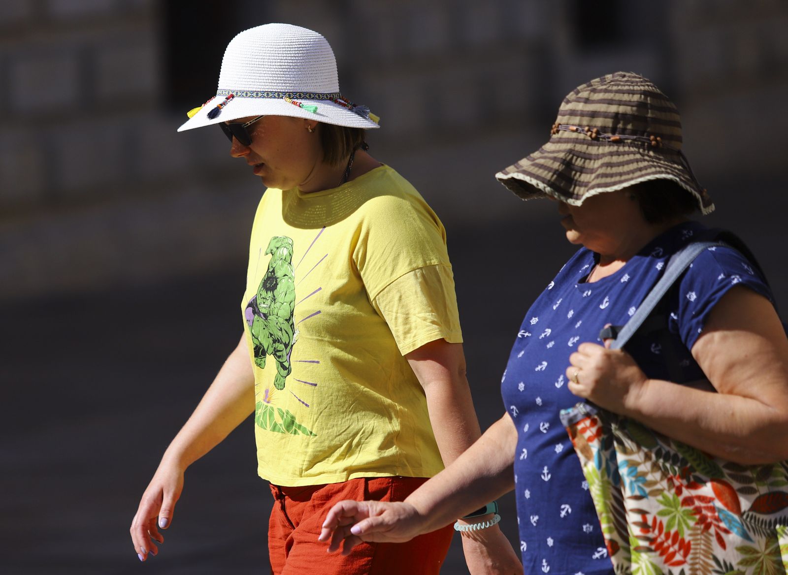 Dos mujeres se protegen del sol con sombreros en el centro de Málaga.