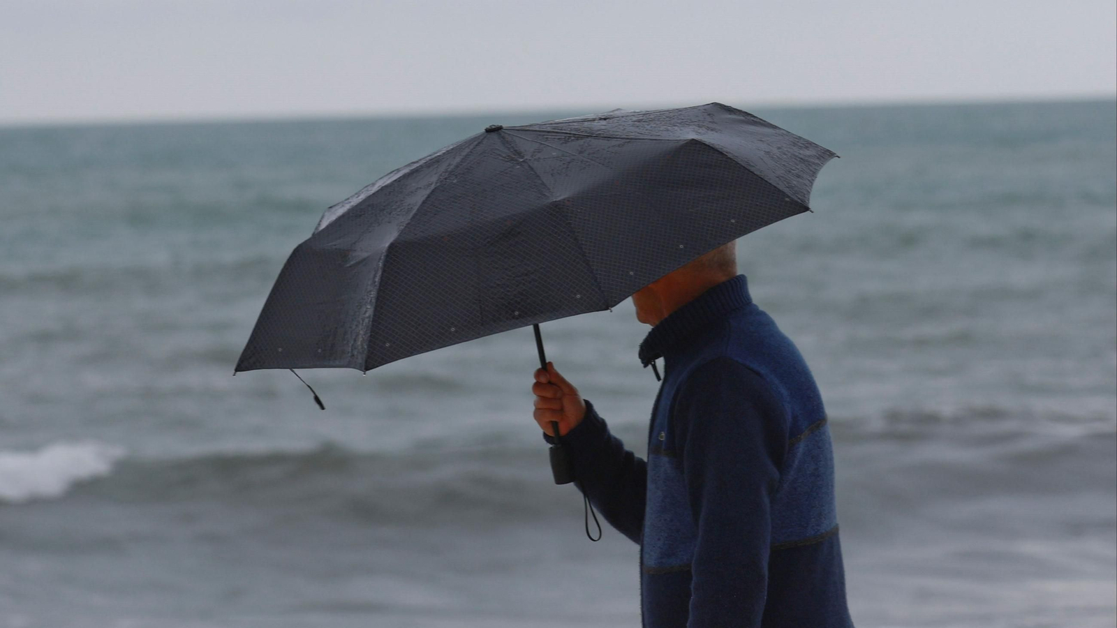 Hombre andando bajo la lluvia en la playa