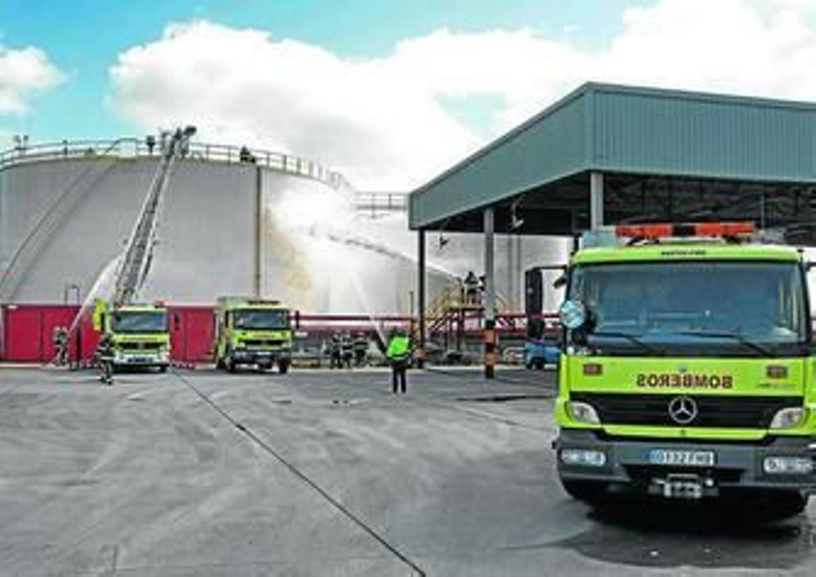 Los bomberos lanzan chorros de agua hacia el tanque durante la práctica de incendio, ayer en la terminal de CLH.