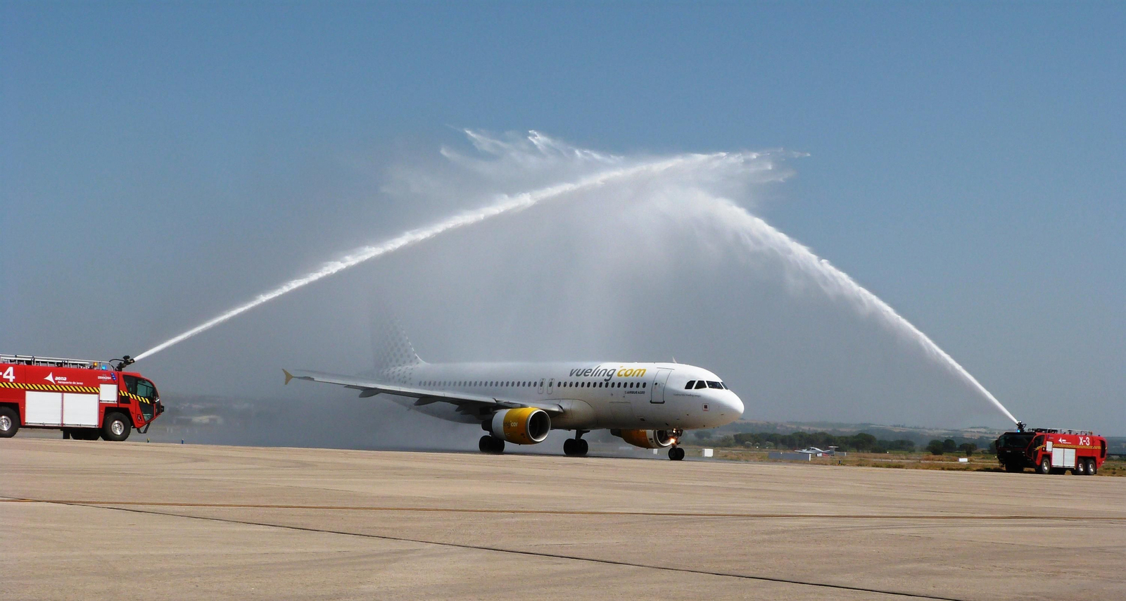 El Airbus 320 de Vueling cruza bajo el arco de agua que provocan los camiones de Bomberos.