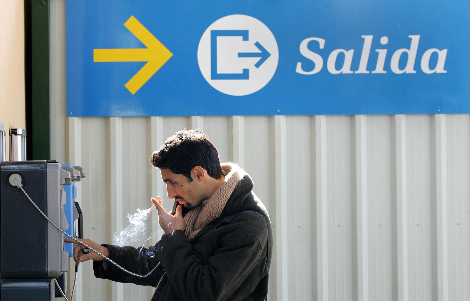 Un fumador habla por un teléfono público mientras sujeta un cigarrillo.