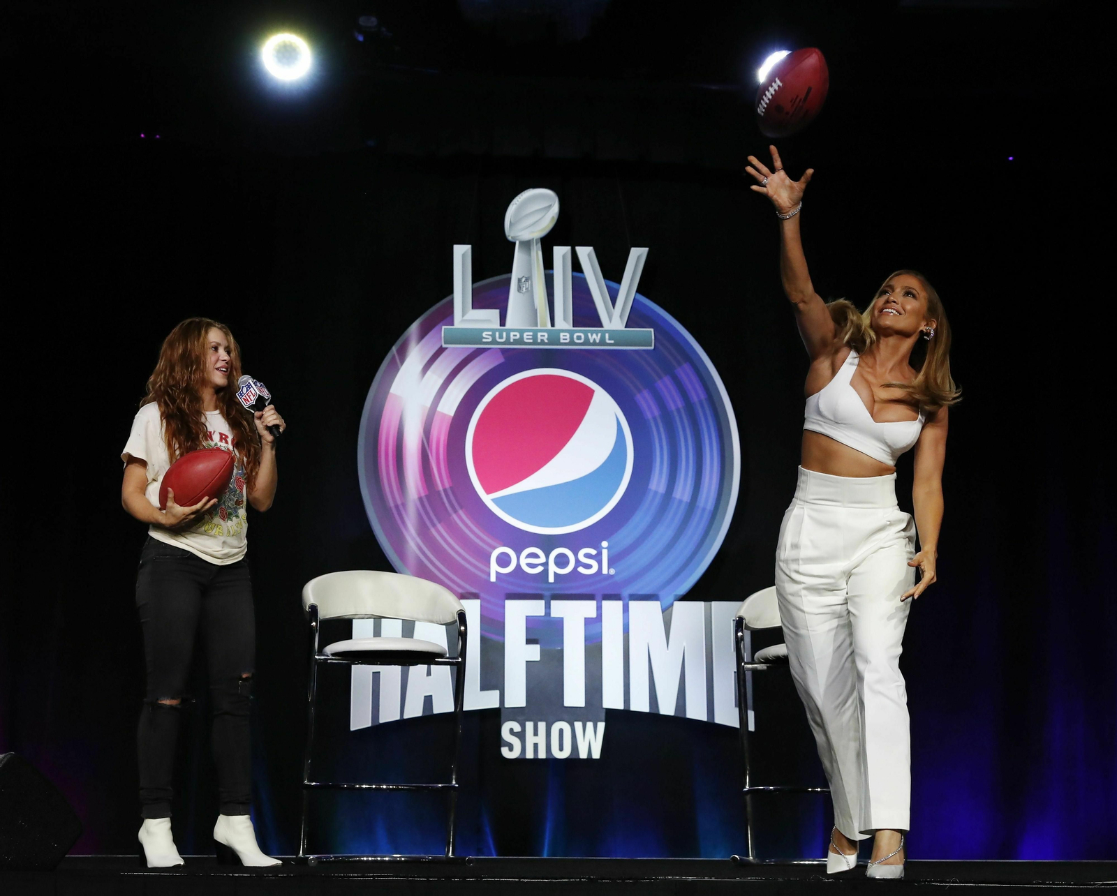 JLo lanza un balón de fútbol americano ante la presencia de Shakira, en la presentación de su 'show' en la 'Superbowl'.