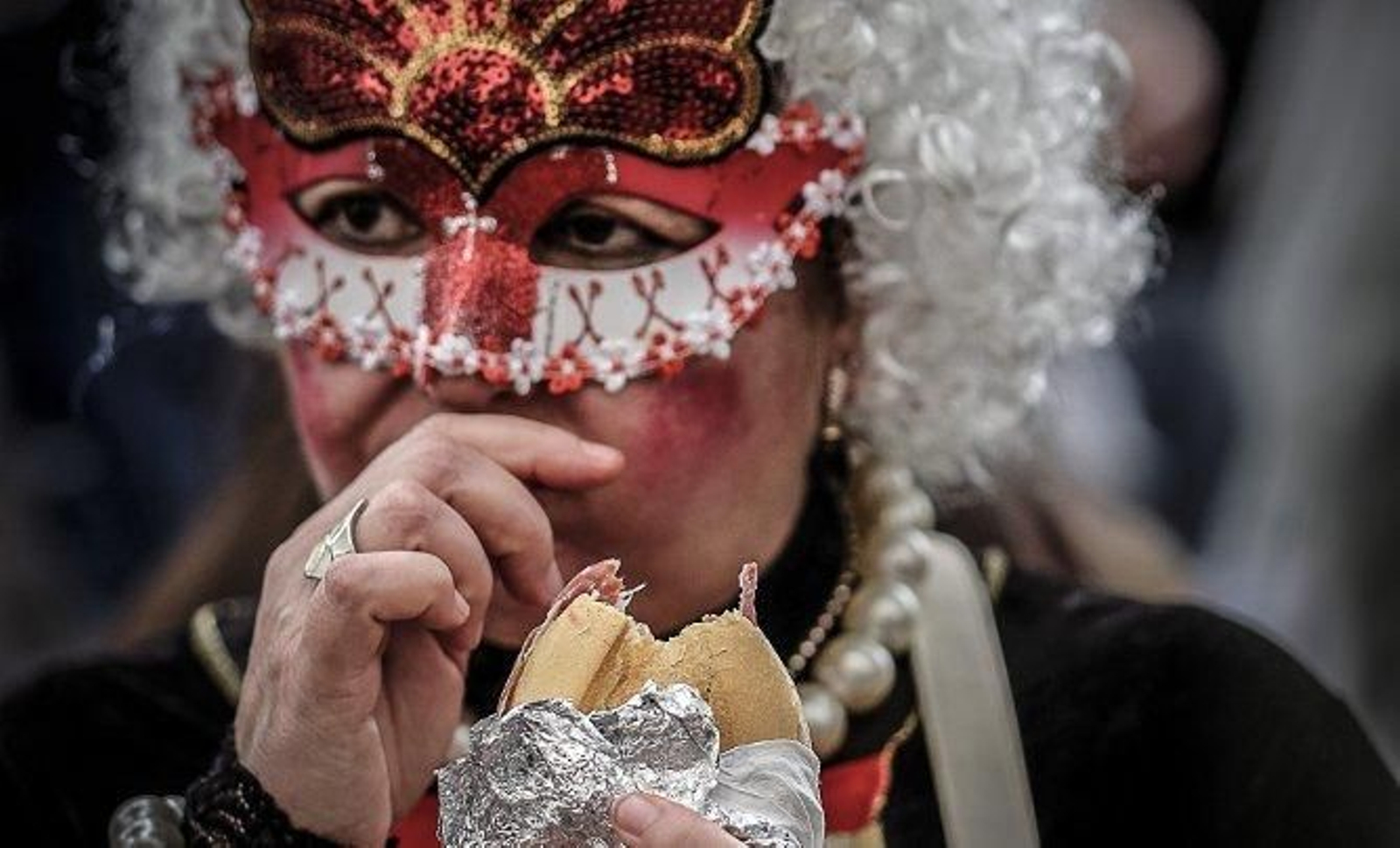 Una mujer, ataviada con un antifaz, se come un bocadillo durante el Carnaval.