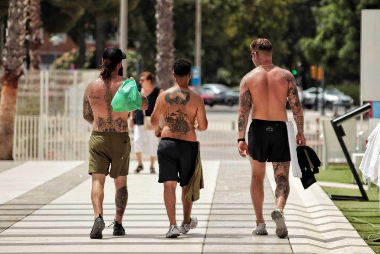 Tres jóvenes sin camiseta pasean por Málaga.