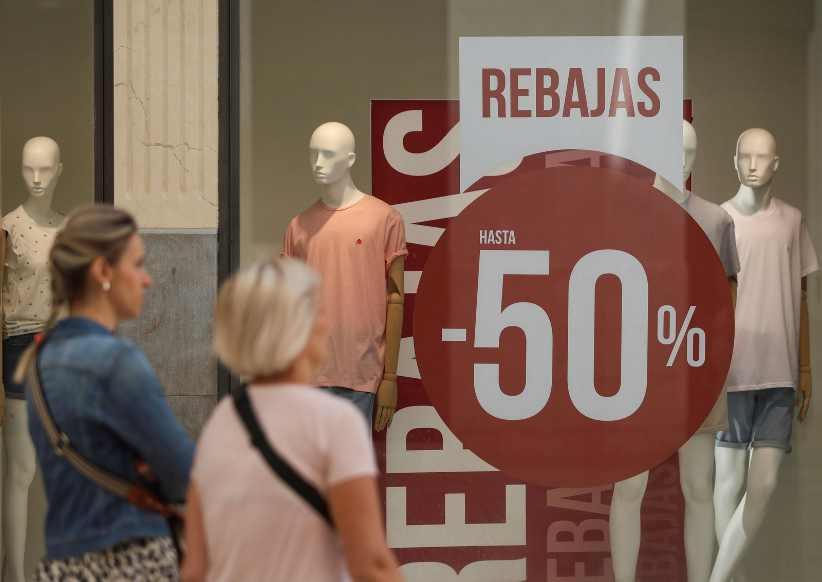 Viandantes pasan junto a un cartel que anuncia rebajas en Málaga. Viandantes pasan junto a un cartel que anuncia rebajas en Málaga.