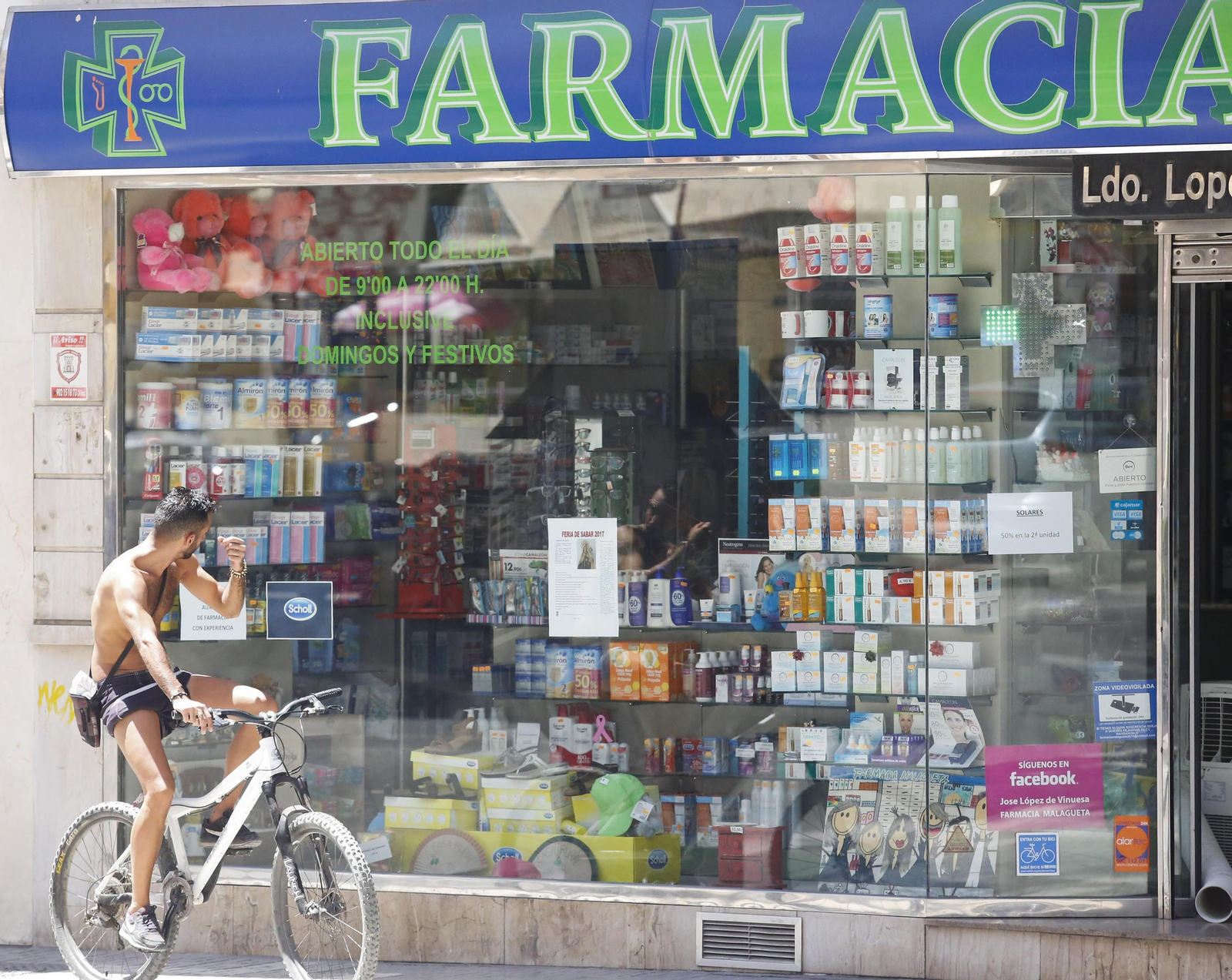 Un ciclista pasa delante de una farmacia.