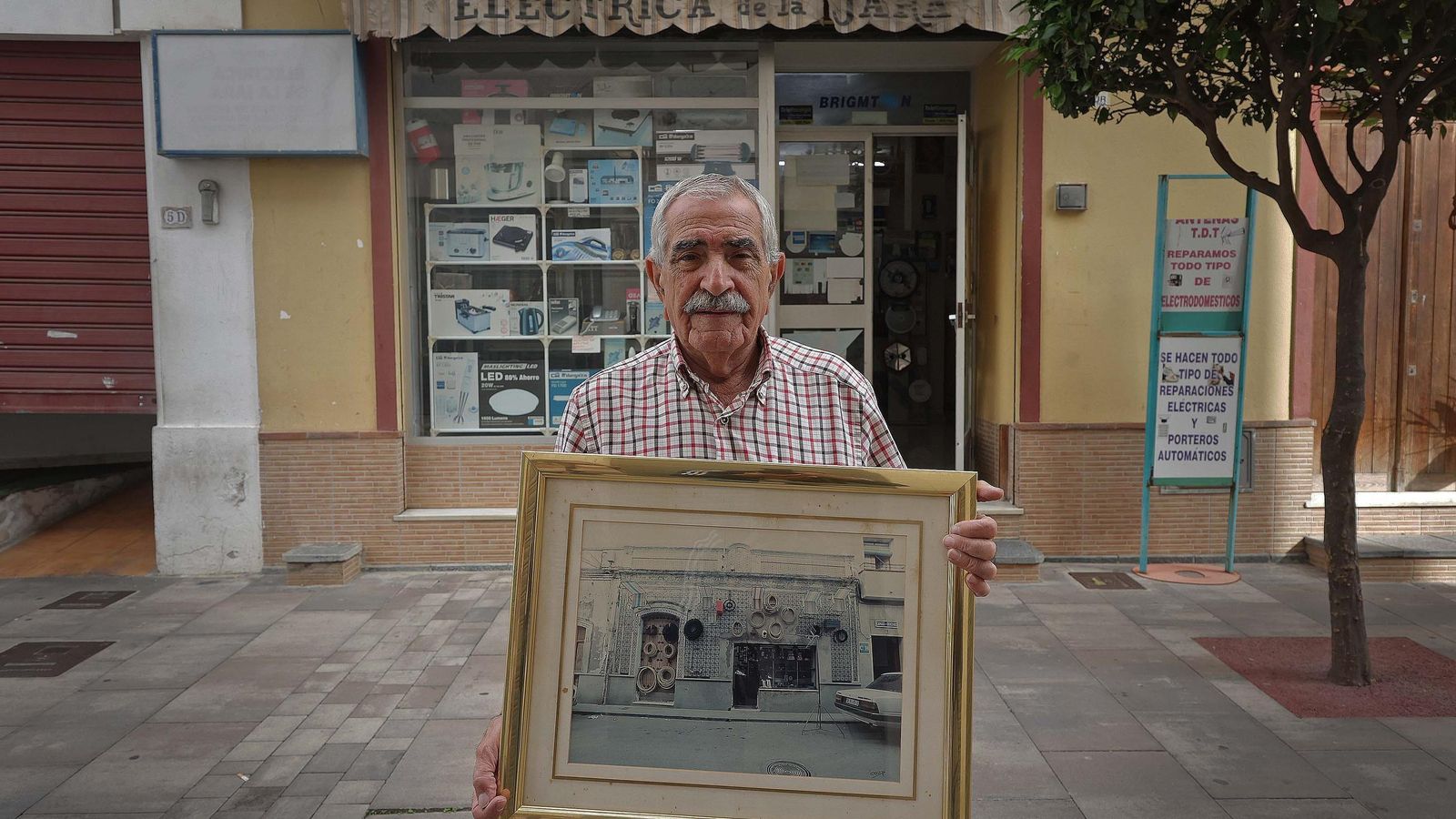 Francisco de la Jara en la calle Duque de Almodóvar, con la foto de la tienda cuando empezó en 1952.