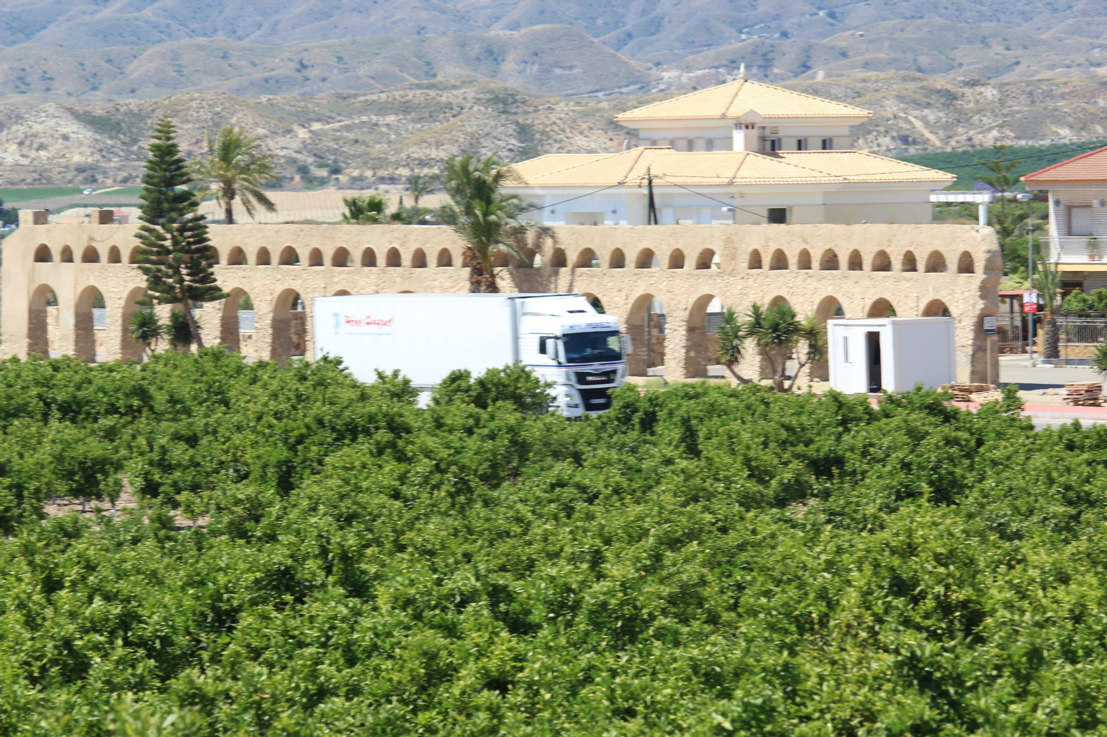 Un camión de una empresa de transporte antense circula junto al acueducto y un campo de naranjos. Un camión de una empresa de transporte antense circula junto al acueducto y un campo de naranjos.