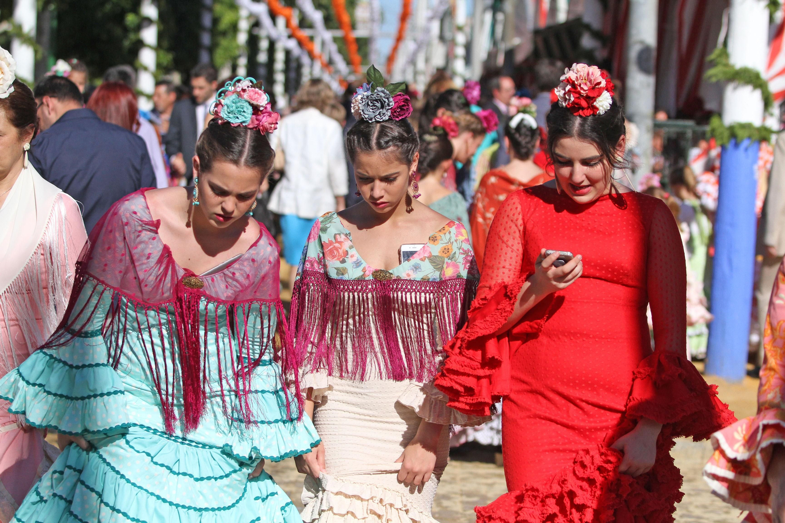 Tres jóvenes vestidas de flamenca atraviesan el real de Los Remedios en la pasada edición de la Feria de Abril.
