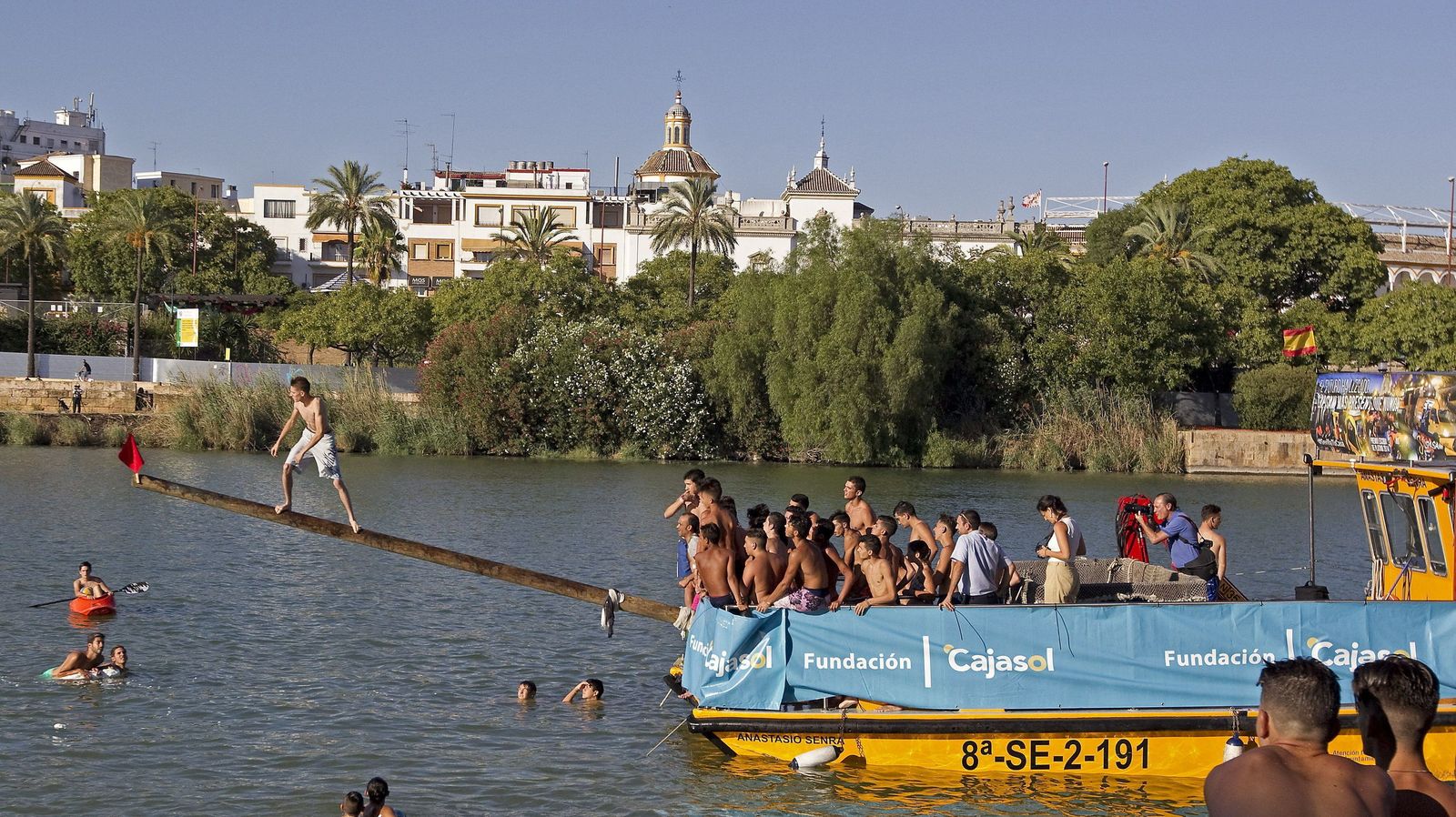 Un joven alcanza la bandera de la Cucaña, en el río Guadalquivir, una de las actividades que se celebran con motivo de la Velá  Santa  Ana.