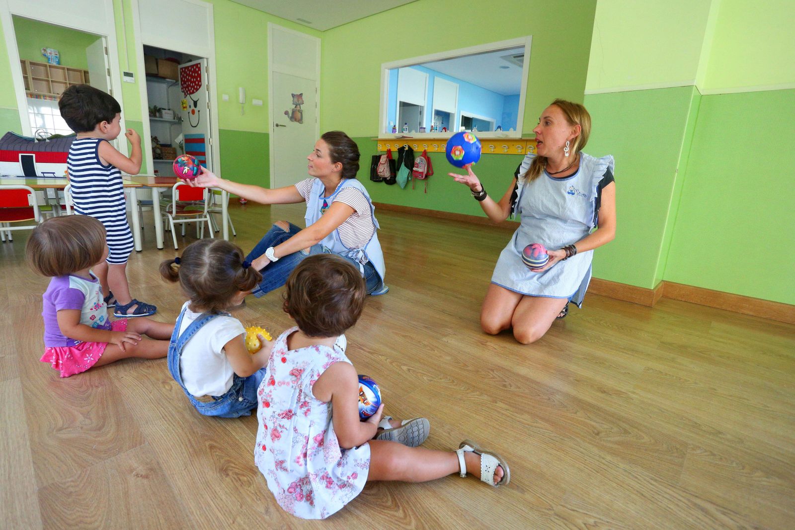 Un grupo de niños atiende a las explicaciones de las trabajadoras de una escuela infantil.