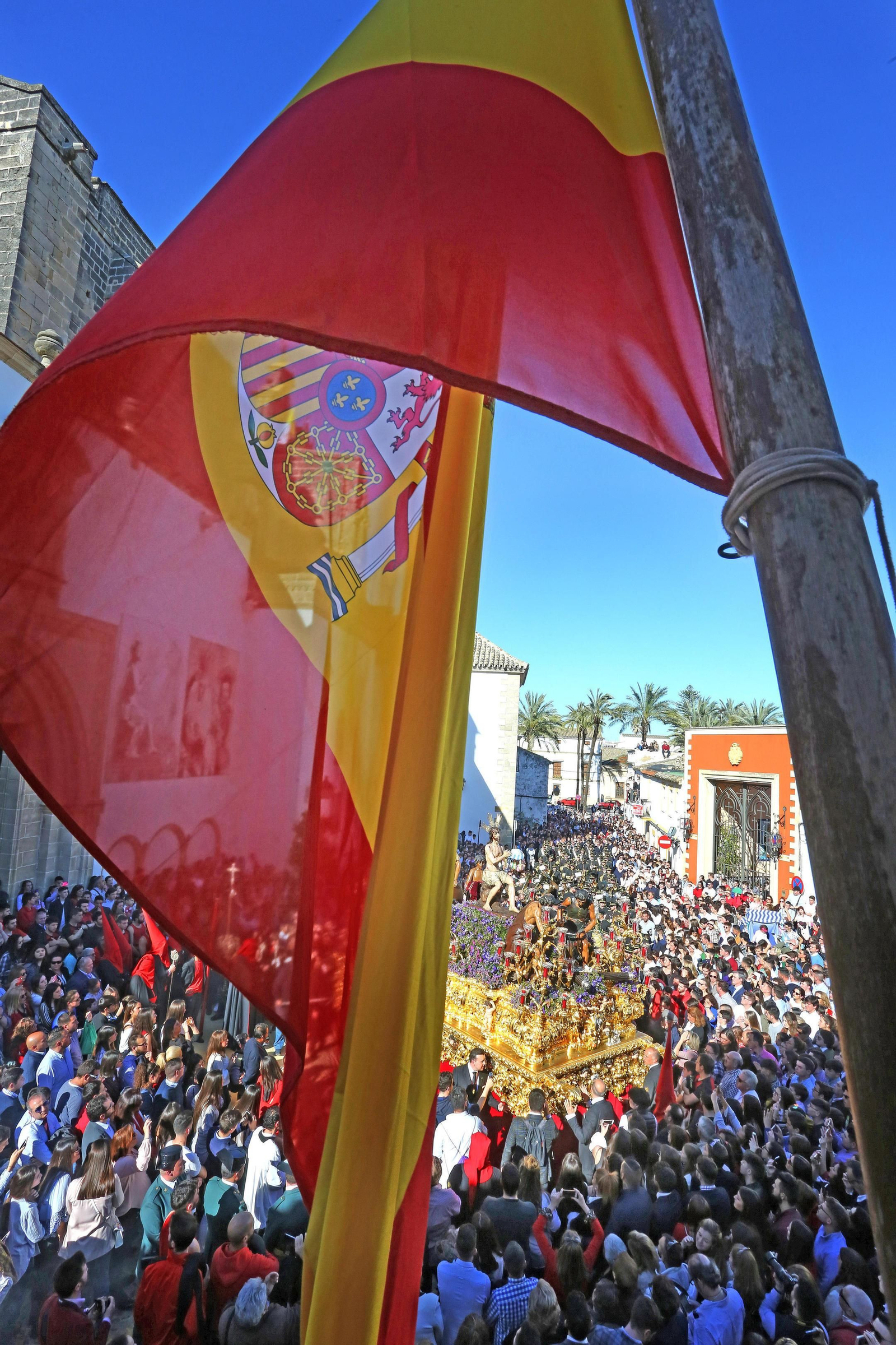 La bandera de España ondeando en el balcón de la casa de hermandad de los Judíos con el paso de misterio de fondo.