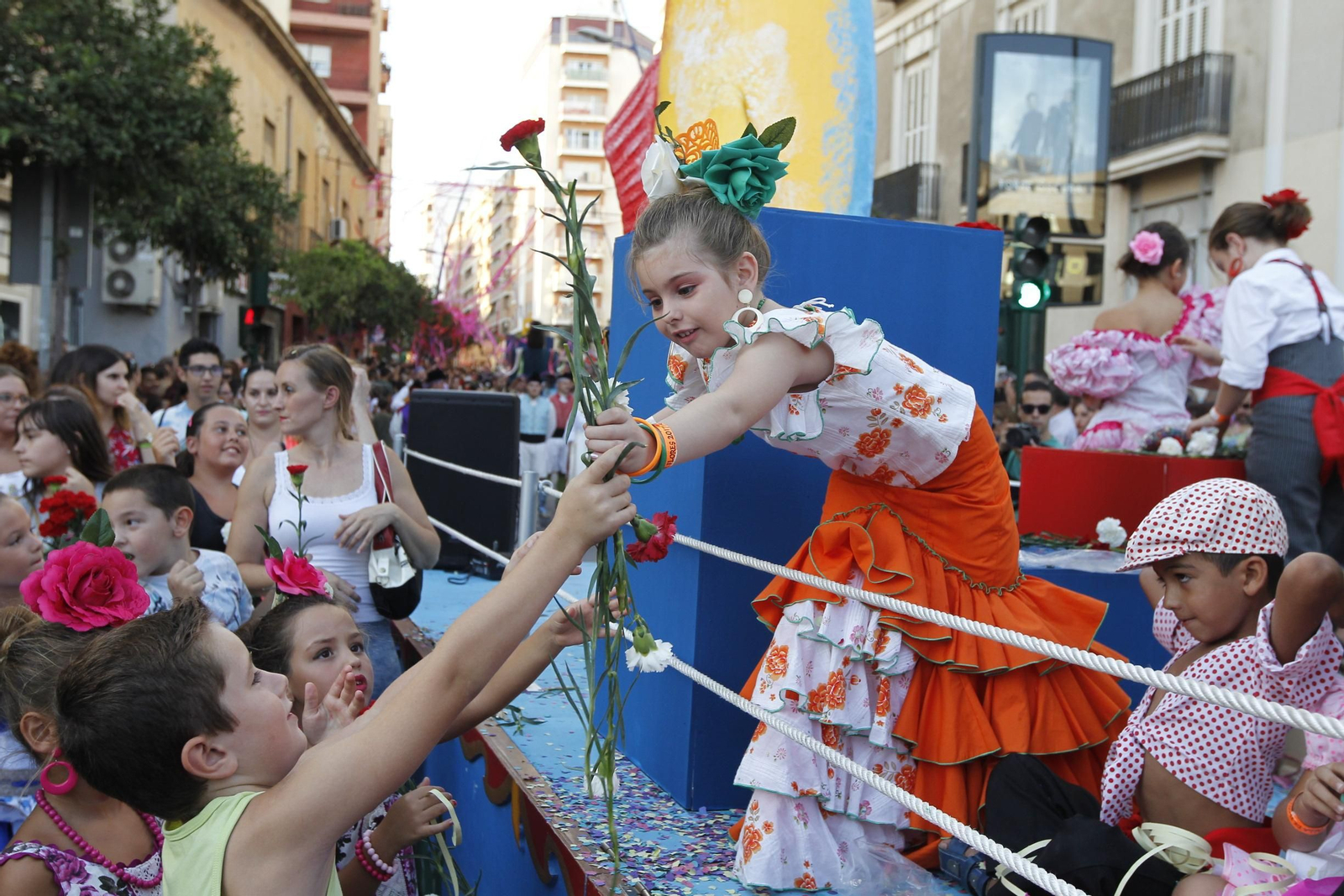 Una niña entrega claveles desde una de las carrozas de la Feria de Almería.