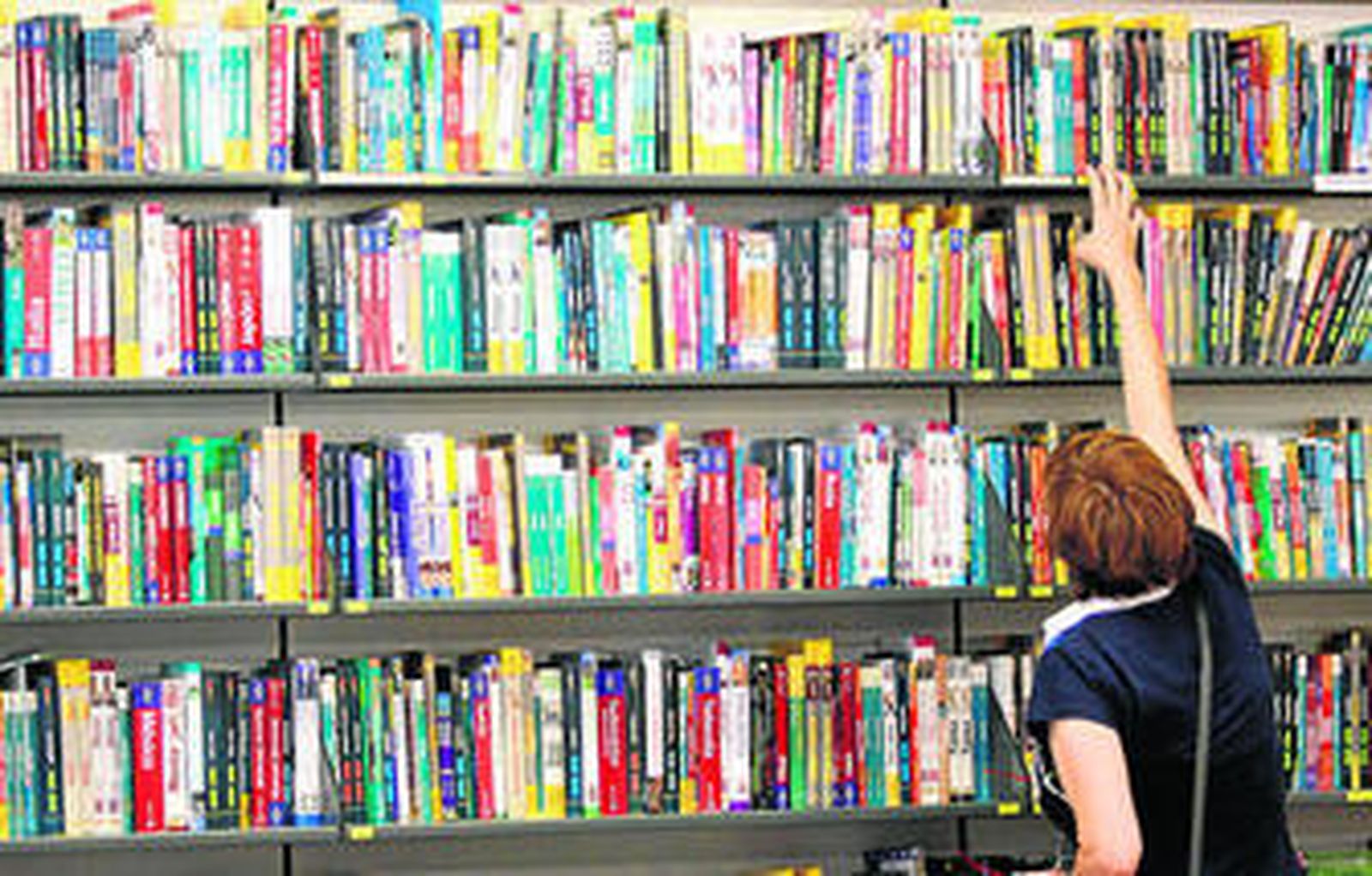 Una mujer busca un libro en una estantería.