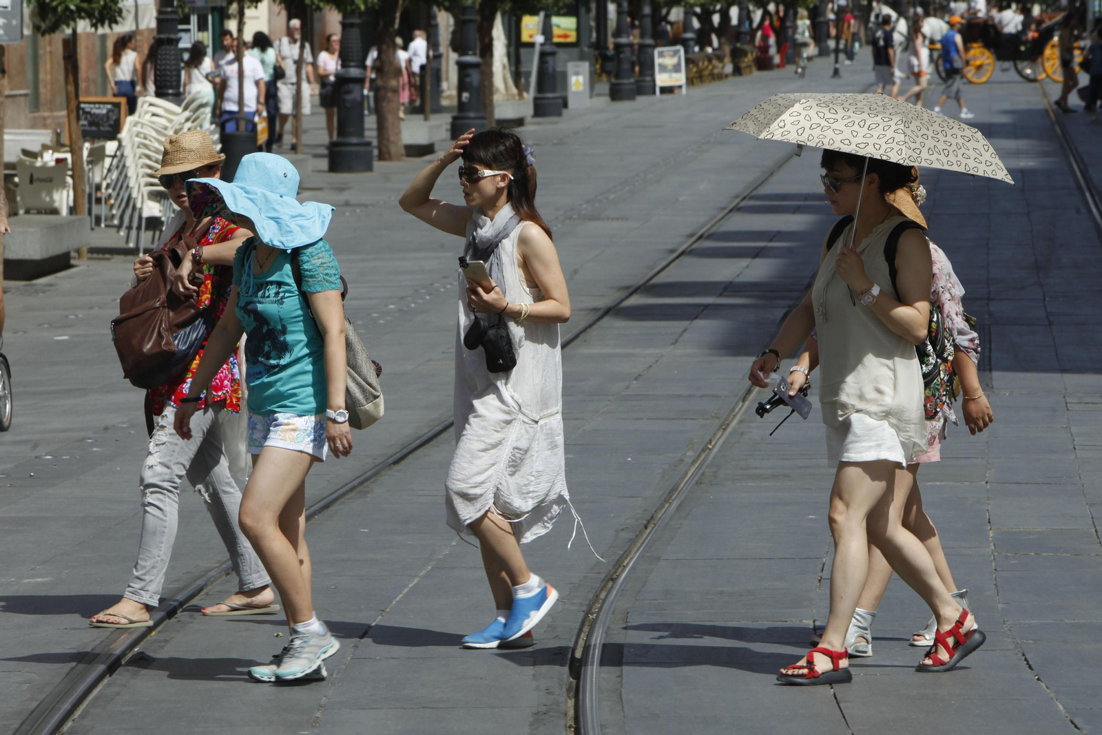 Turistas paseando por la Avenida de la Constitución con paraguas para protegerse del calor