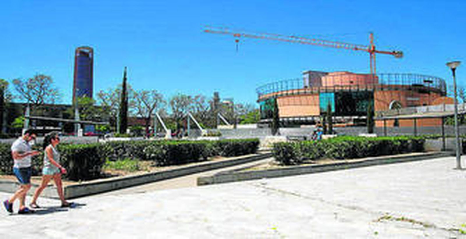 Dos peatones cruzan por la plaza inhóspita y sin sombra como está ahora.