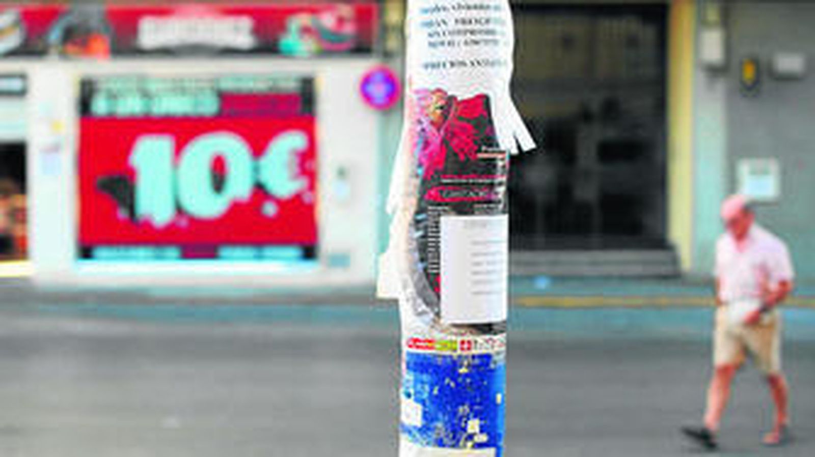 En la imagen, una farola del centro de la ciudad con varios carteles pegados en toda su superficie.