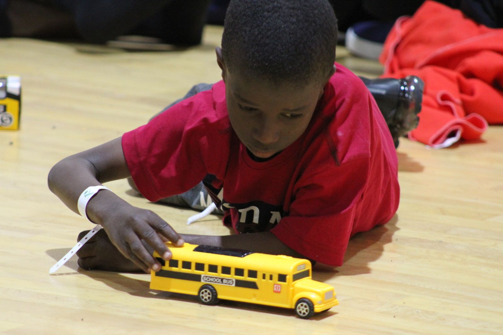 Un menor, una vez identificado, descansa sobre la pista del pabellón polideportivo de Barbate, jugando con un autobús escolar.