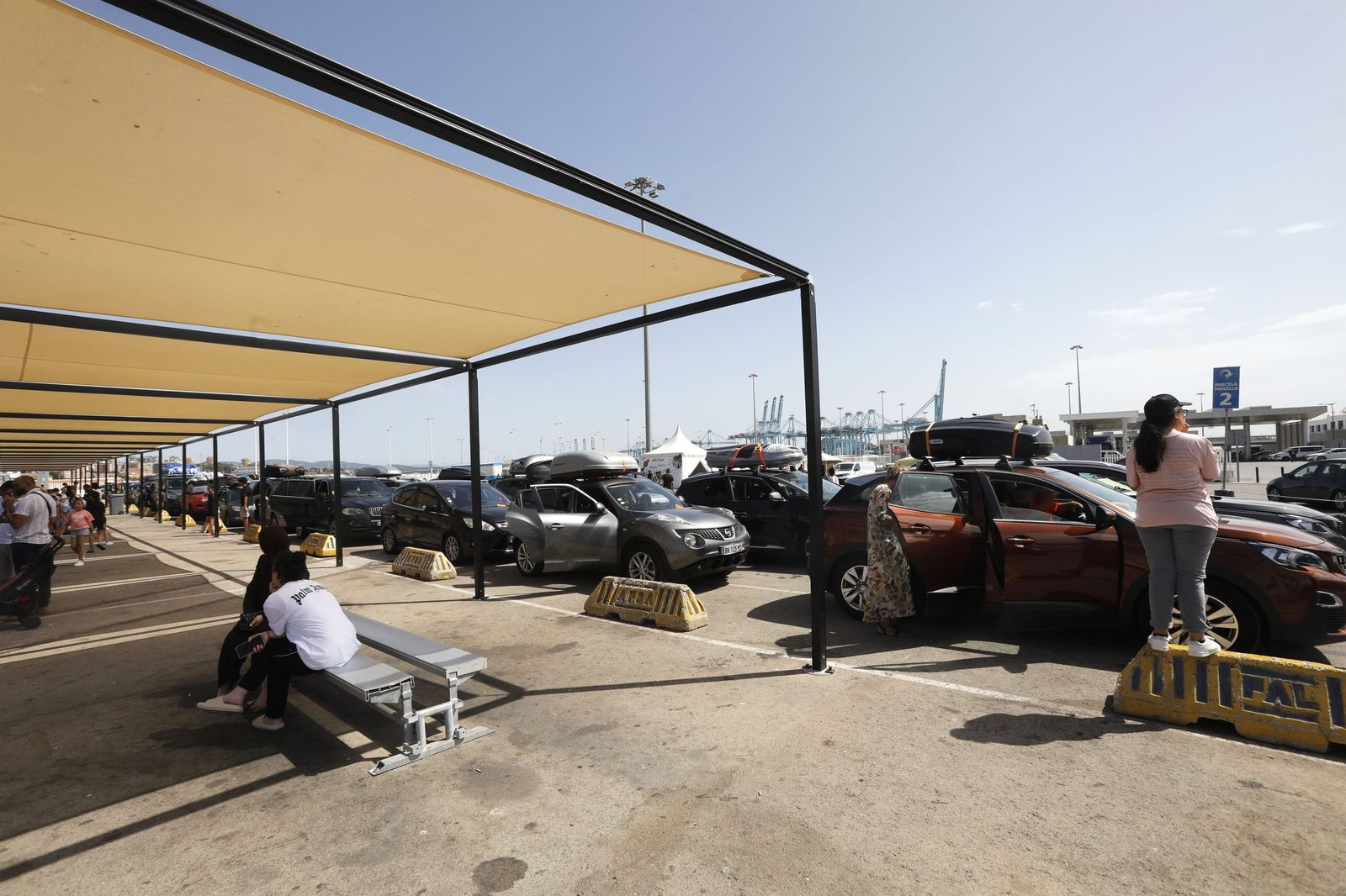 Los viajeros esperan su turno debajo de una sombra para embarcar, en Algeciras.