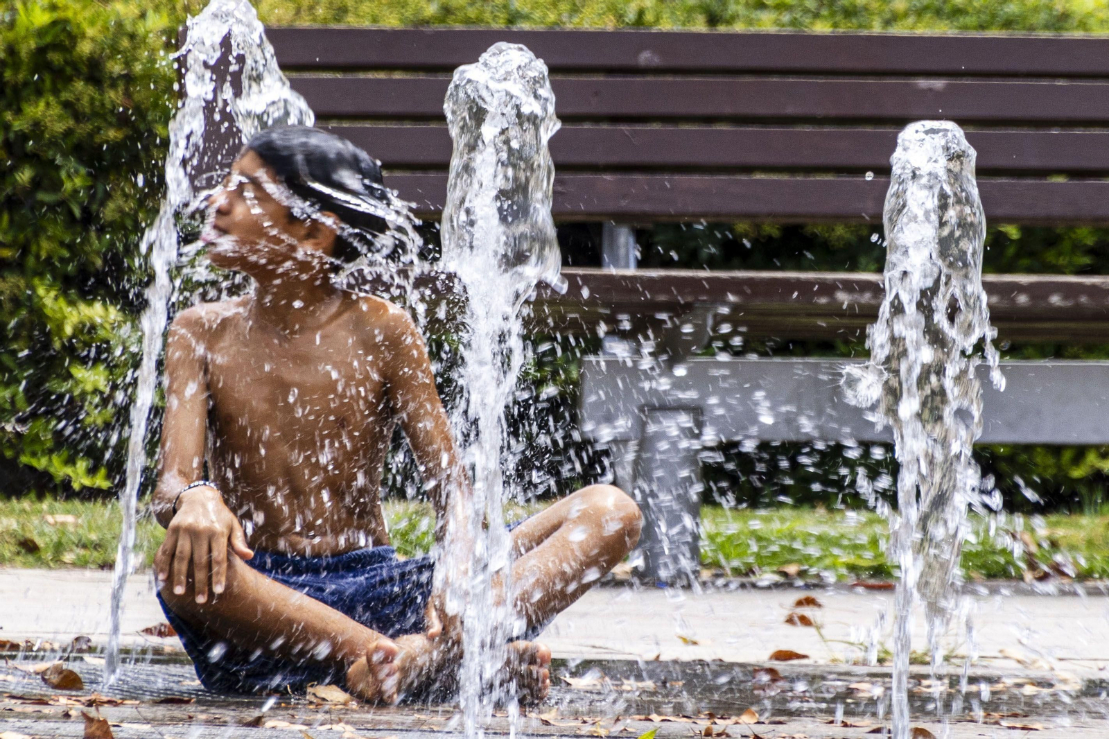 Un joven se refresca en una fuente.