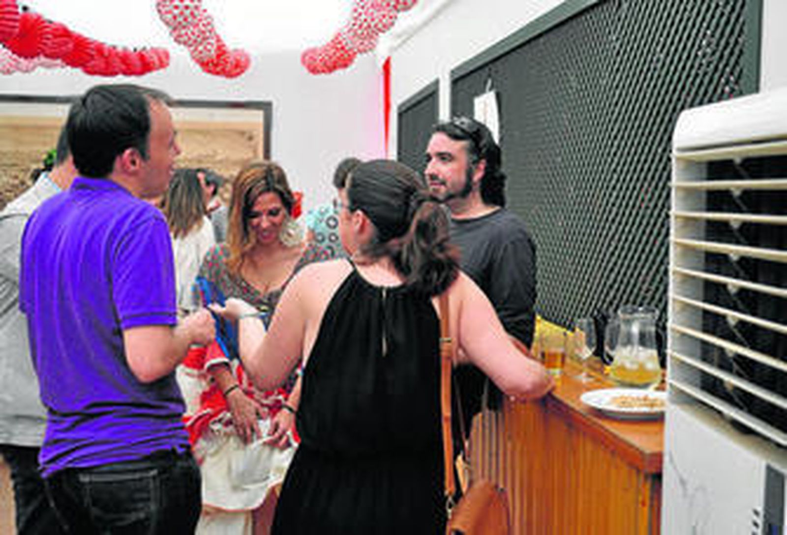 Un grupo de jóvenes disfrutan de la Feria en la caseta de la Asociación de la Prensa de Sevilla, delante de un aparato de climatización.