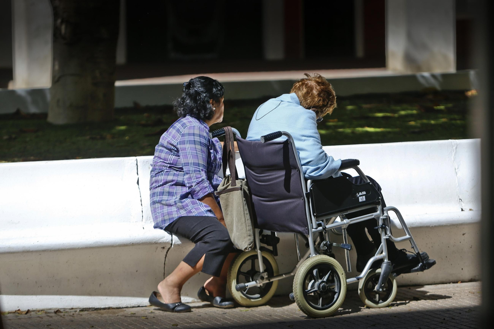 Una persona en silla de rueda acompañada de un familiar.