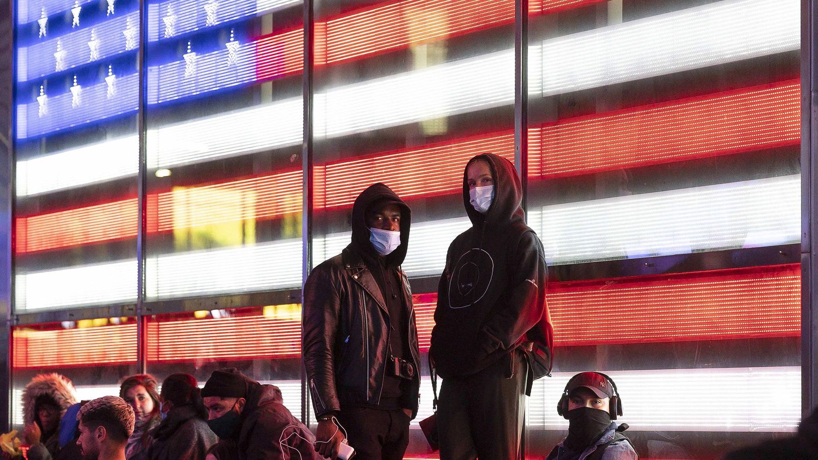 Varios votantes delante de una pantalla led con la bandera de los EEUU