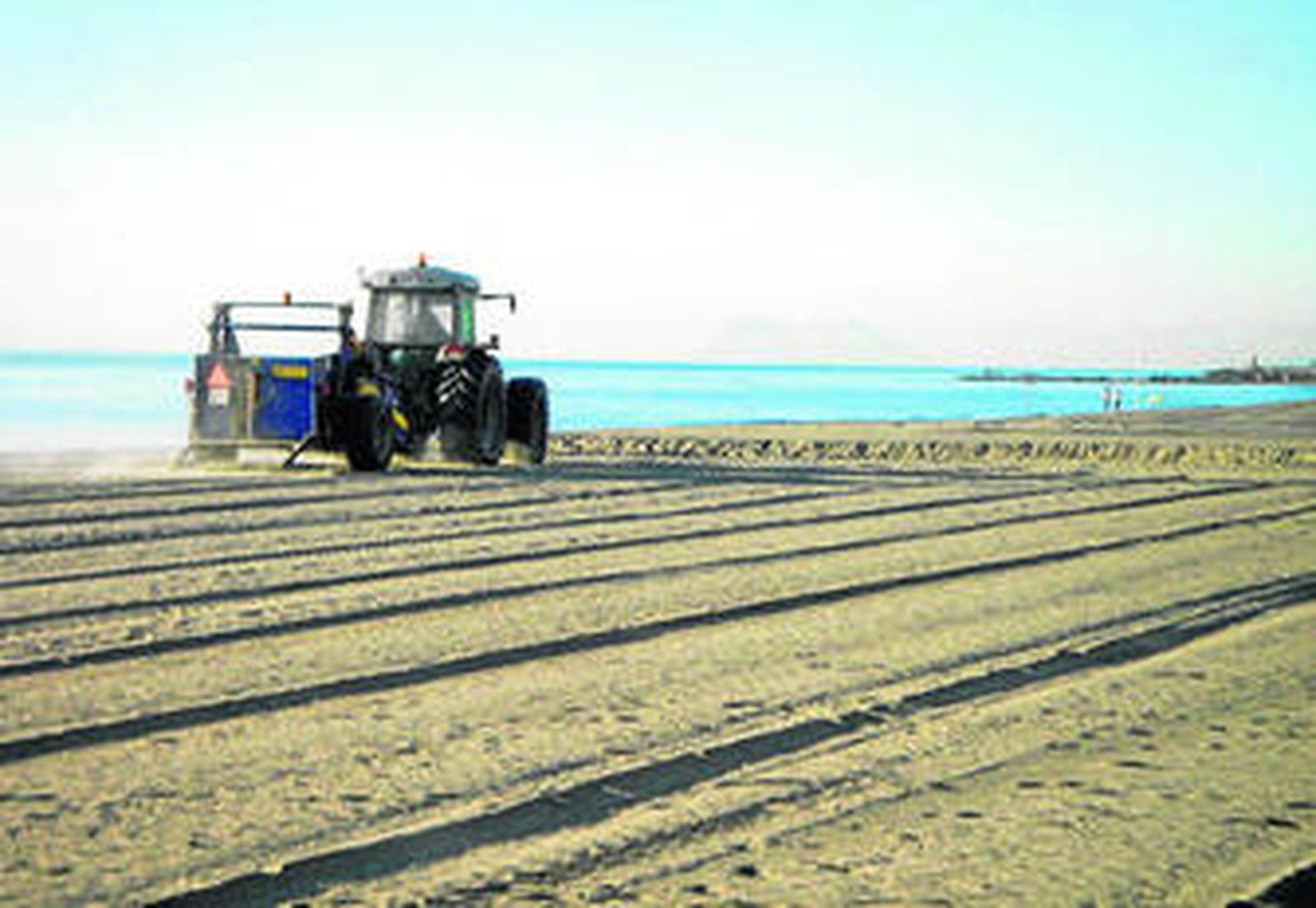 Un tractor allana la arena en la playa de La Rada.