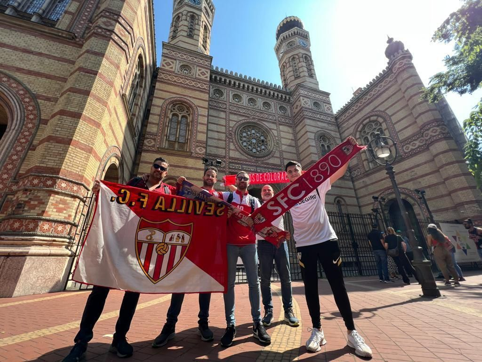 Aficionados sevillistas posan con un fuerte sol.