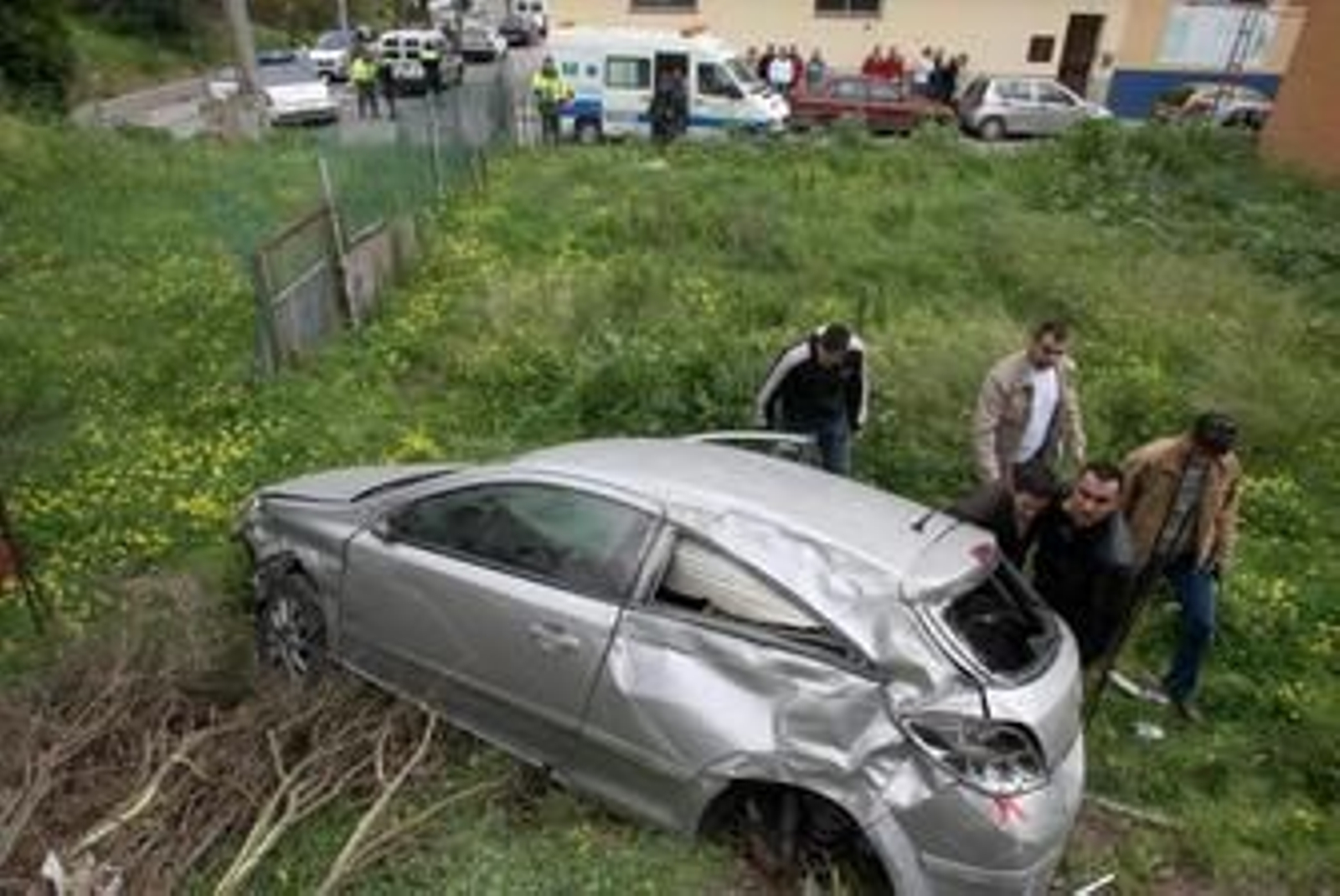 El Opel Astra tras el accidente, mientras vecinos ayudan a salir a sus ocupantes.
