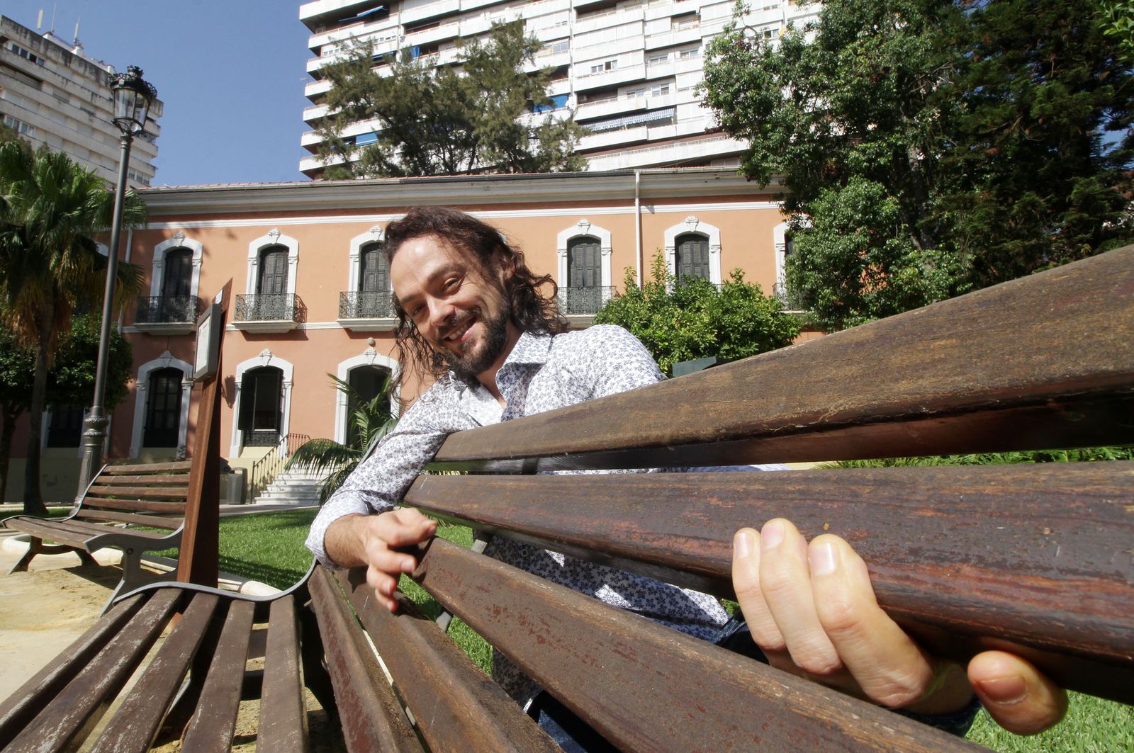El cantante, guitarrista, arreglista y productor onubense Diego Guerrero posa para la entrevista con un banco de la Casa Colón a modo de guitarra.