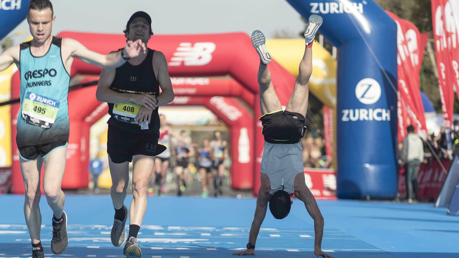 Uno de los corredores hace el pino al llegar a la meta.