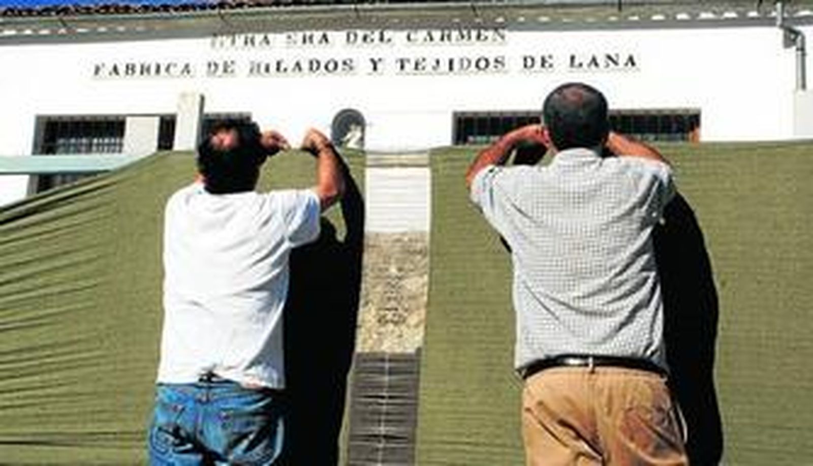 Trabajadores tienden las mantas ante la fachada de la última industria textil de Grazalema.