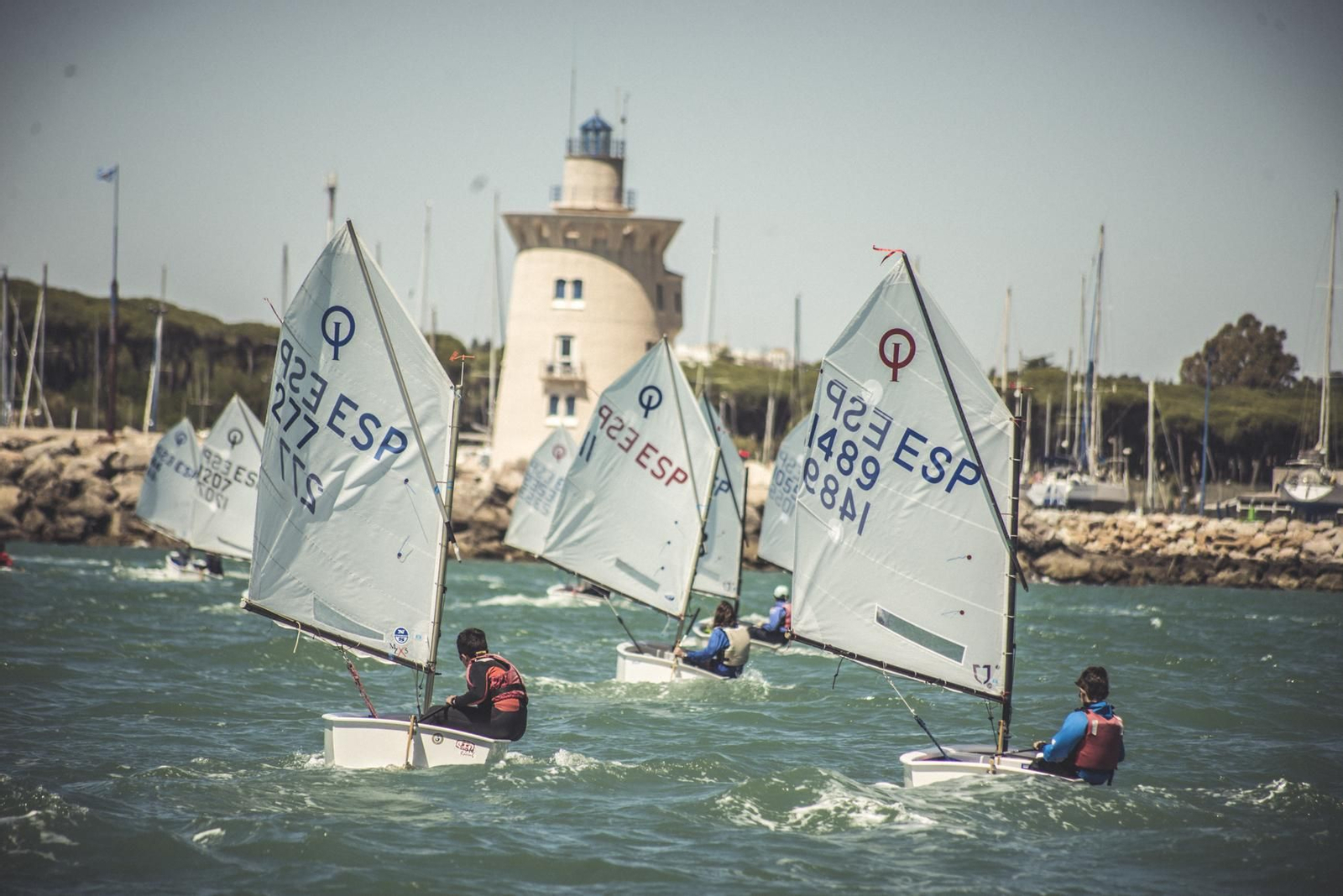 Embarcaciones de la clase Óptimist, en plena regata con el faro de Puerto Sherry al fondo.