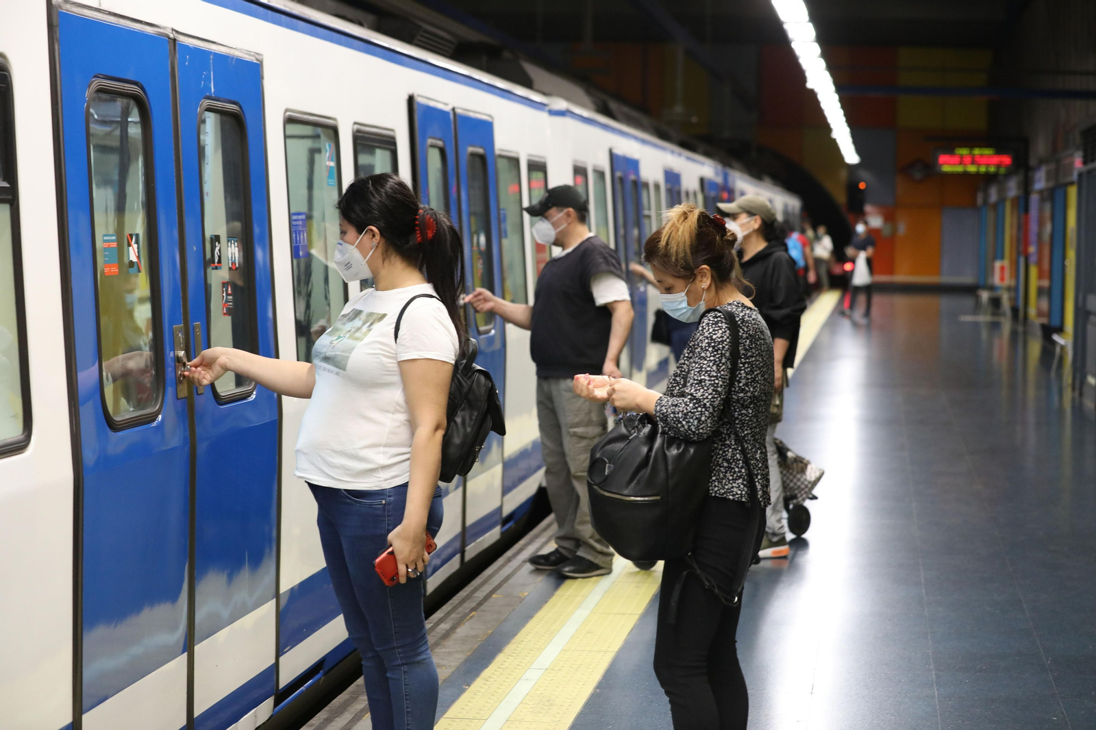Varios pasajeros abreiendo la puerta de un tren del Metro de Madrid.