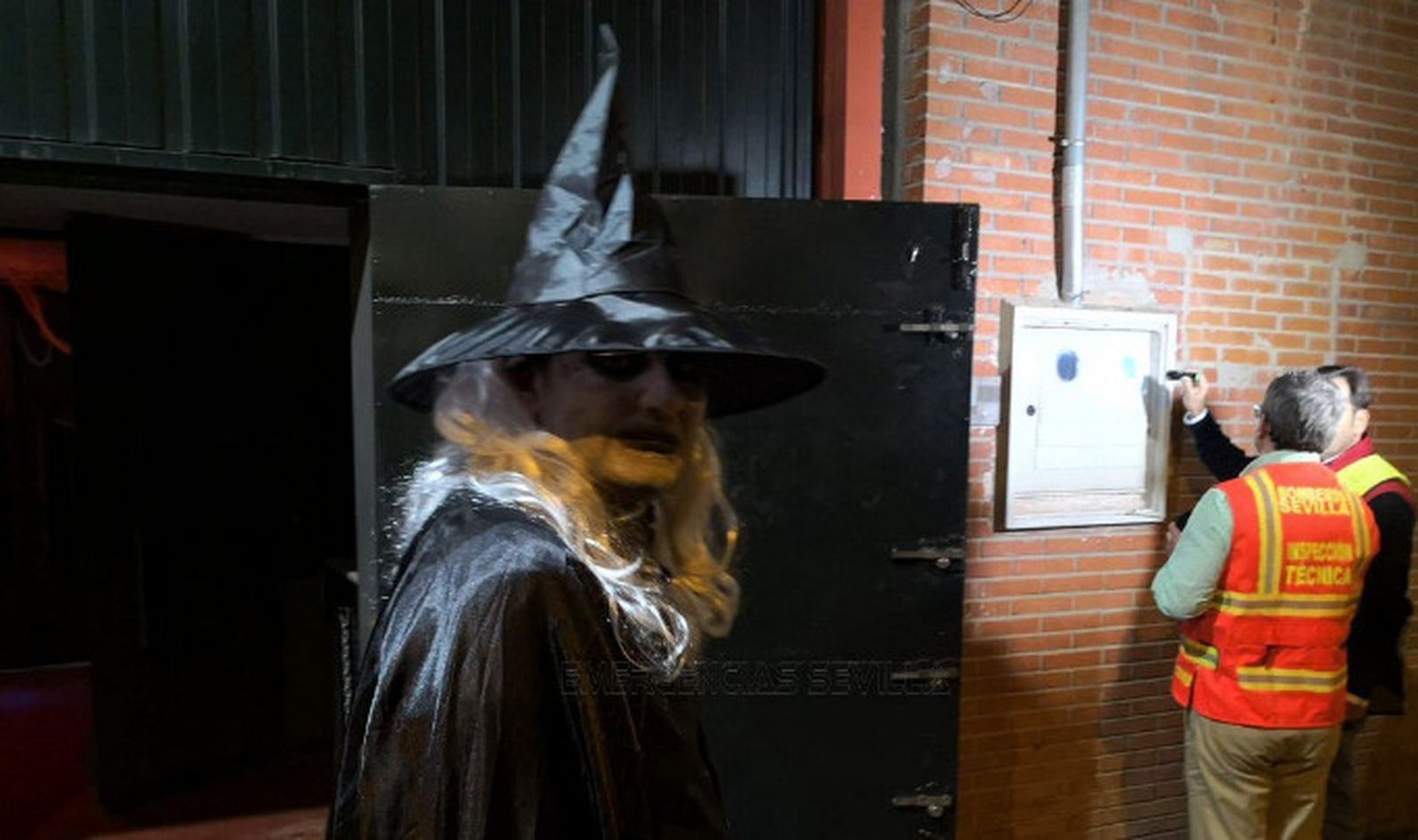 Un joven sale disfrazado de la discoteca mientras los operarios la inspeccionan.