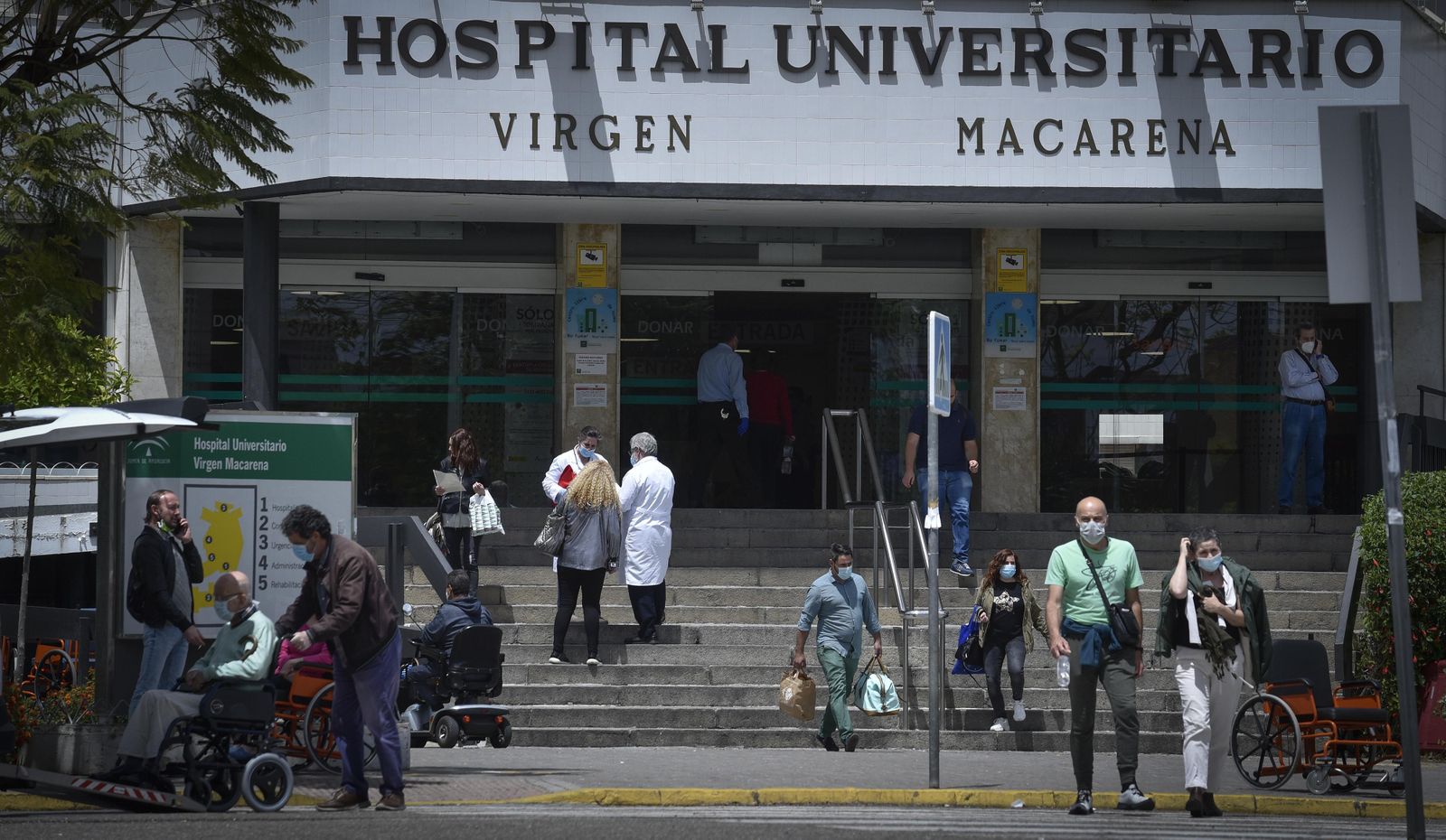 Varias personas y sanitarios coinciden en la puerta principal del Hospital Virgen Macarena.