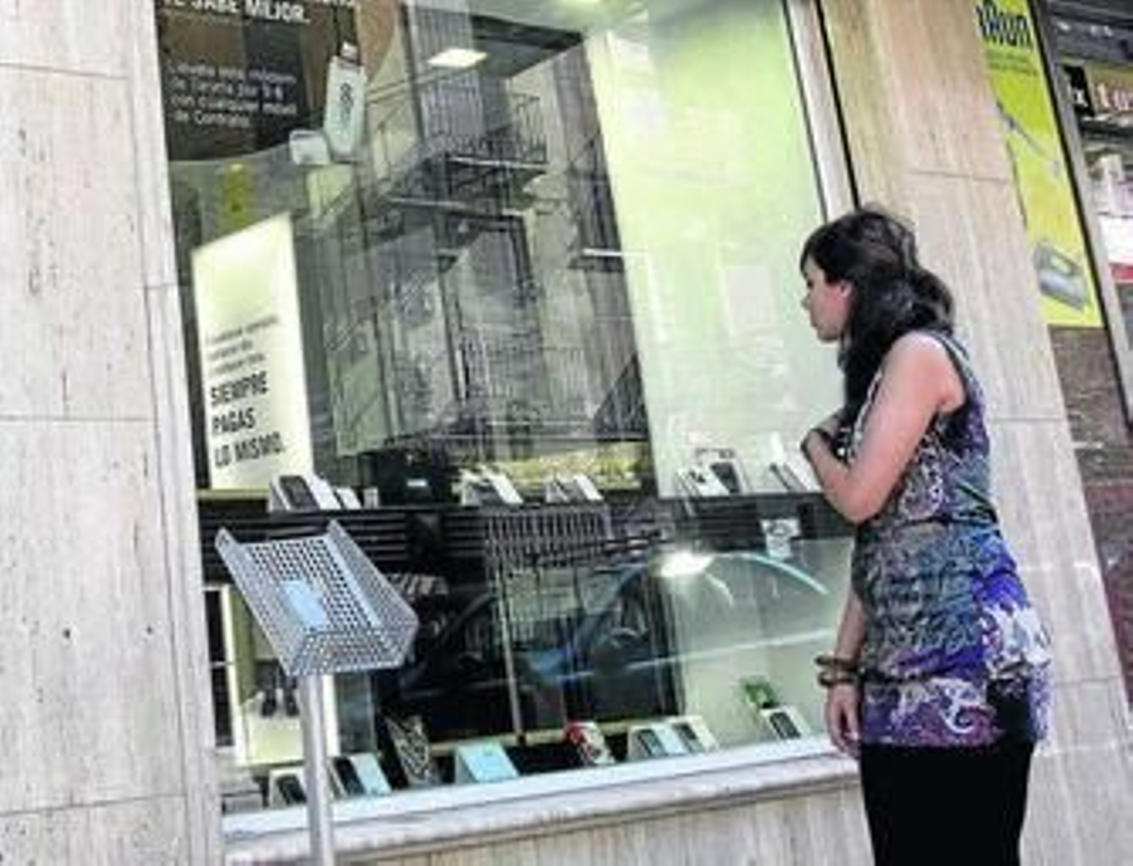 Una joven observa el escaparate de una tienda de telefonía móvil. Una joven observa el escaparate de una tienda de telefonía móvil.