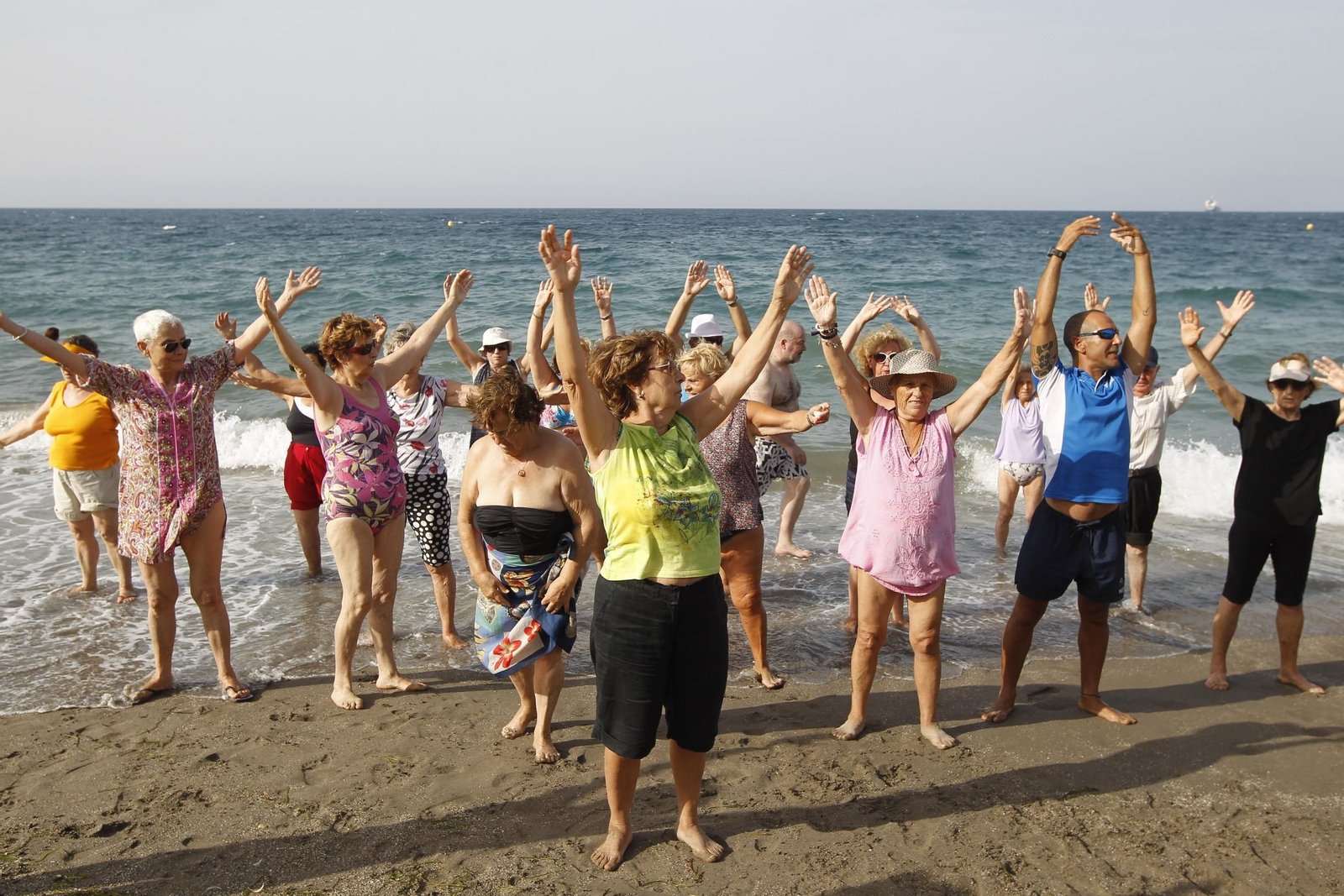 Personas mayores realizando ejercicio físico en la playa.