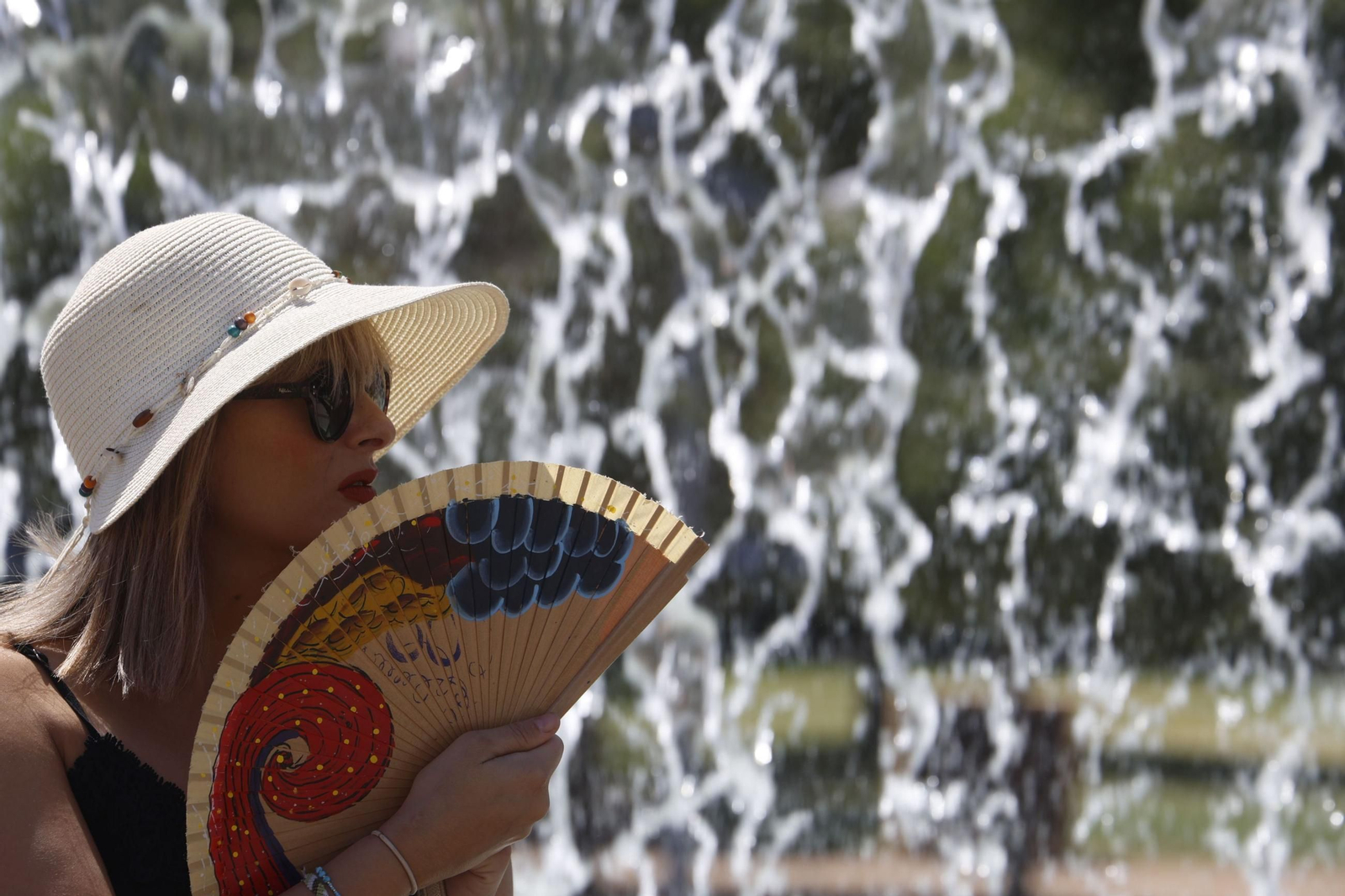 Una mujer se protege del sol en Córdoba con un sombrero mientras se abanica.