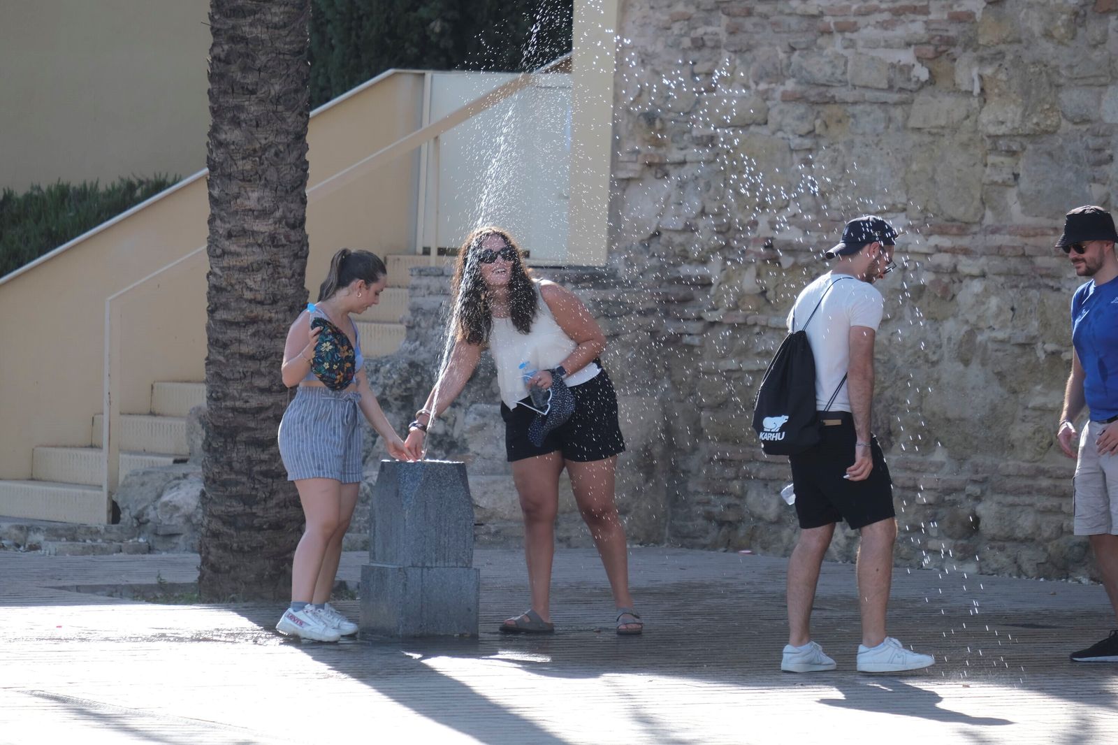 Varias personas se refrescan con una fuente en el entorno de Puerta del Puente.