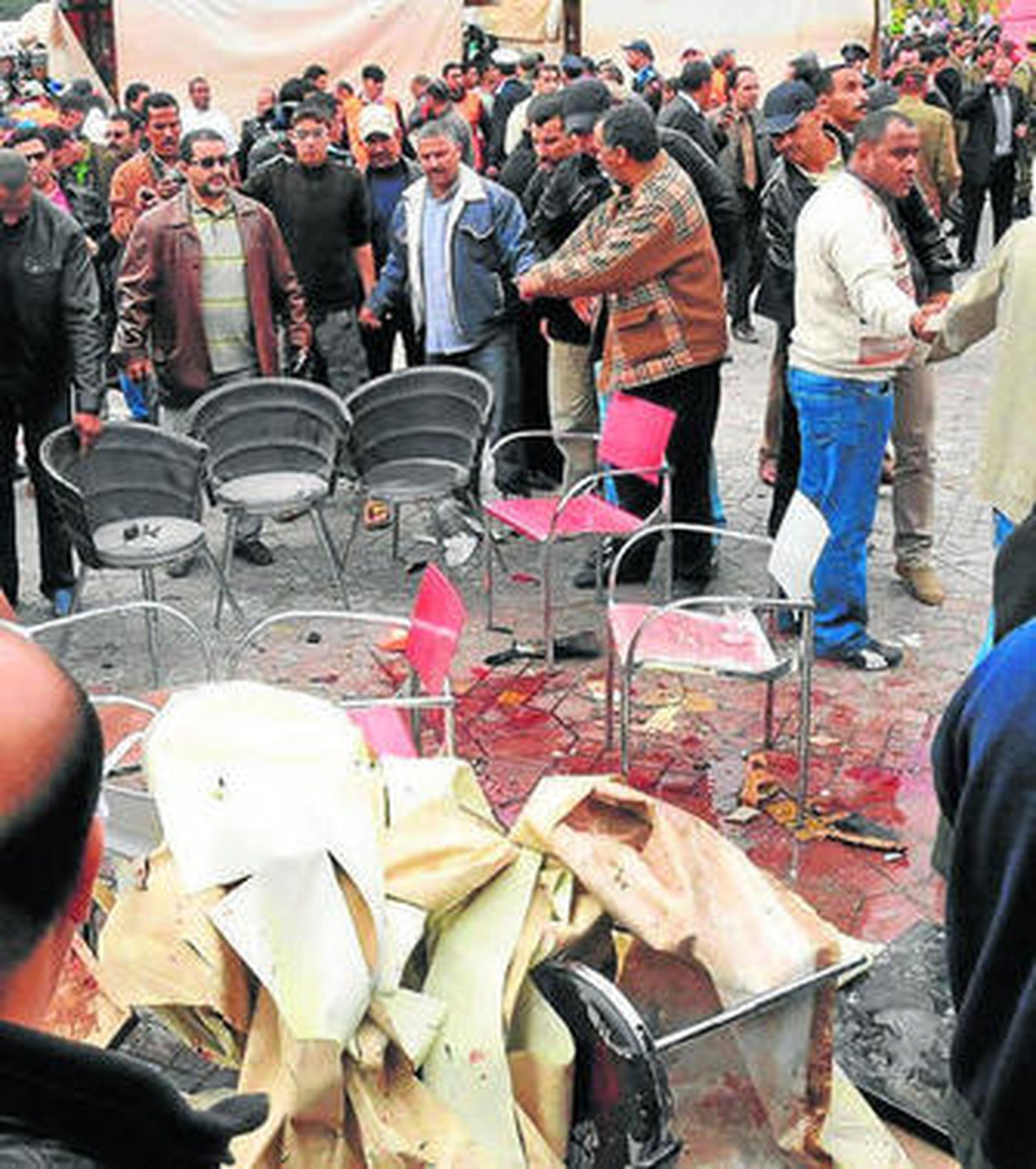 Unos hombres observan el cuerpo de una víctima cubierto con mantas.