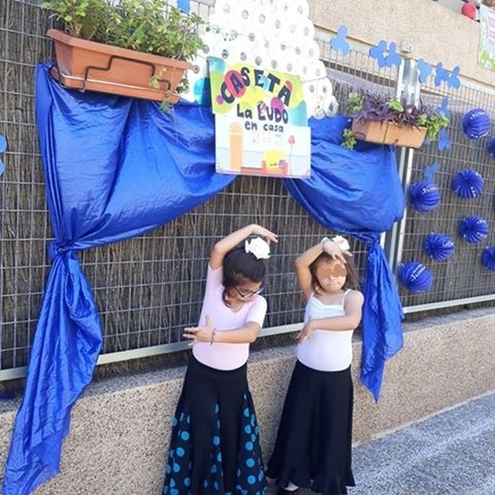 Dos niñas de La Canaleja bailan sevillanas ante la caseta 'La Ludo en Casa'.