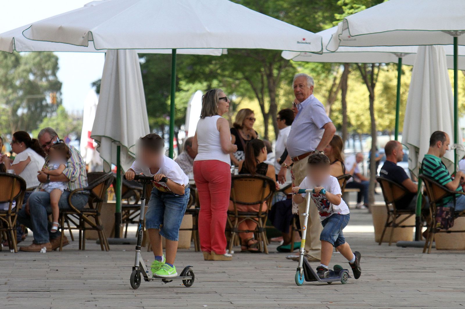 Varios pequeños juegan con sus patinetes ante la mirada de personas mayores.