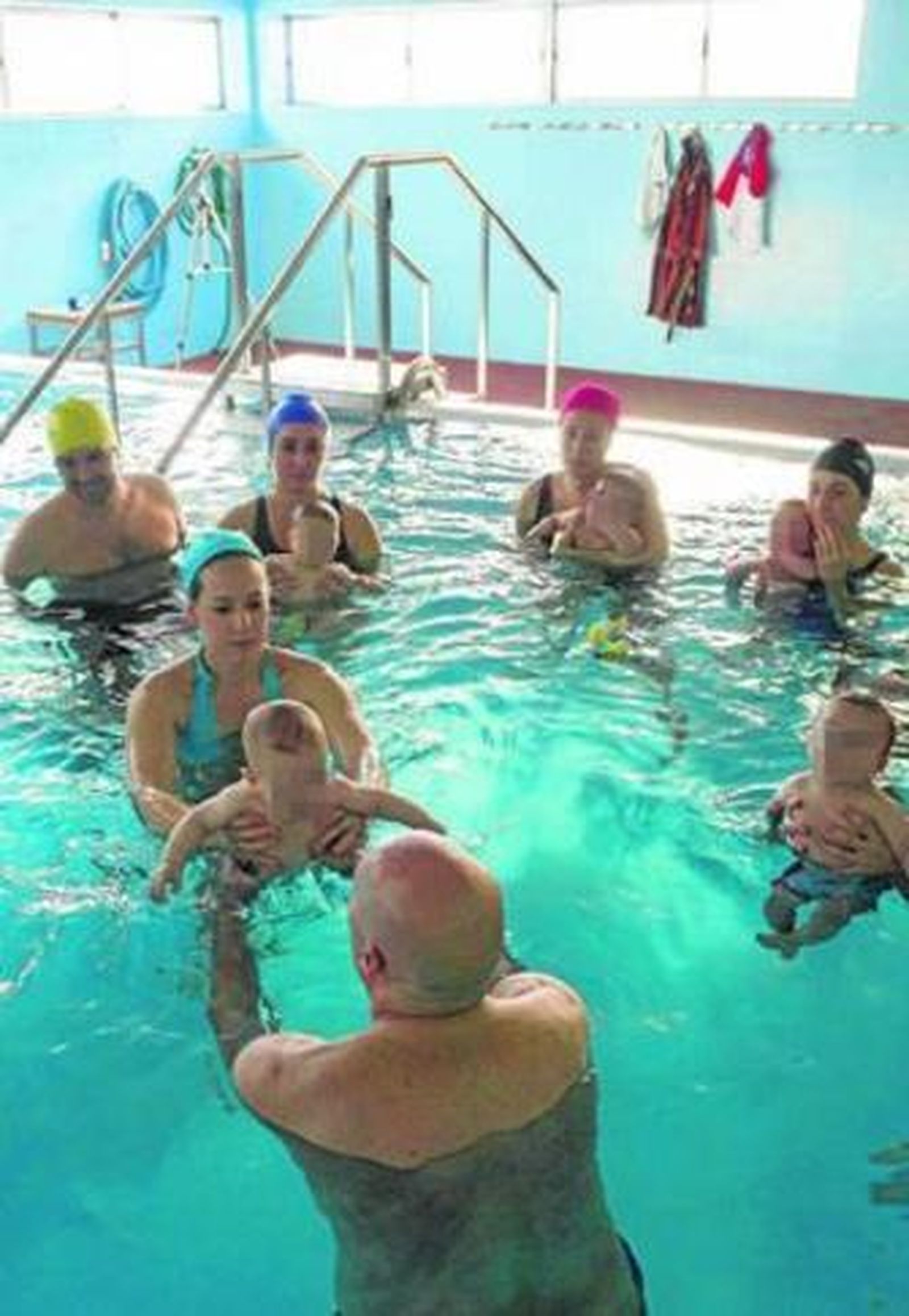 Varios padres disfrutan con sus bebés en una piscina.
