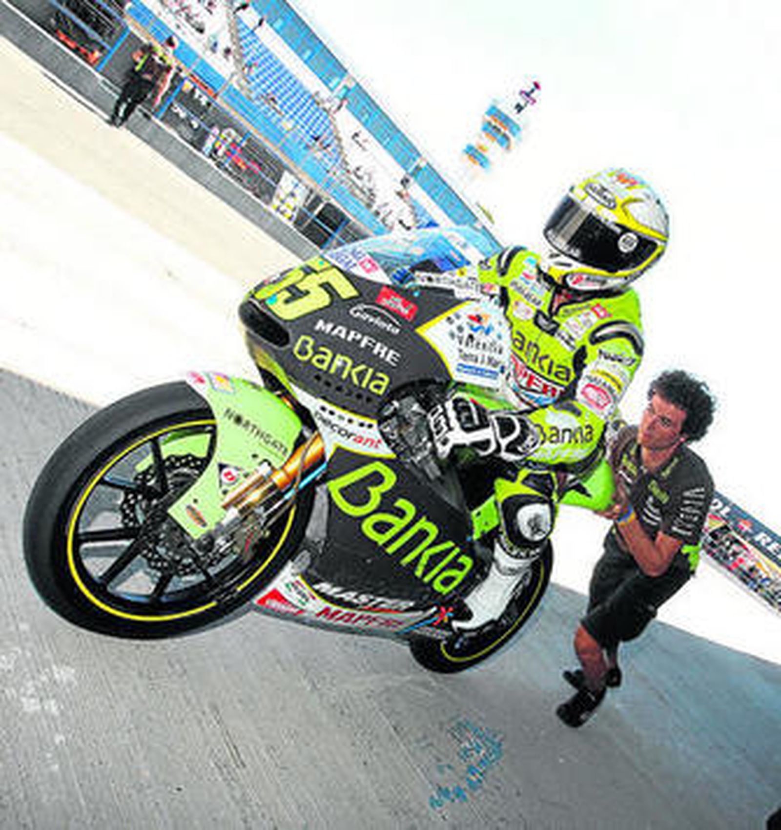 Héctor Faubel arranca su moto con la ayuda de un mecánico.