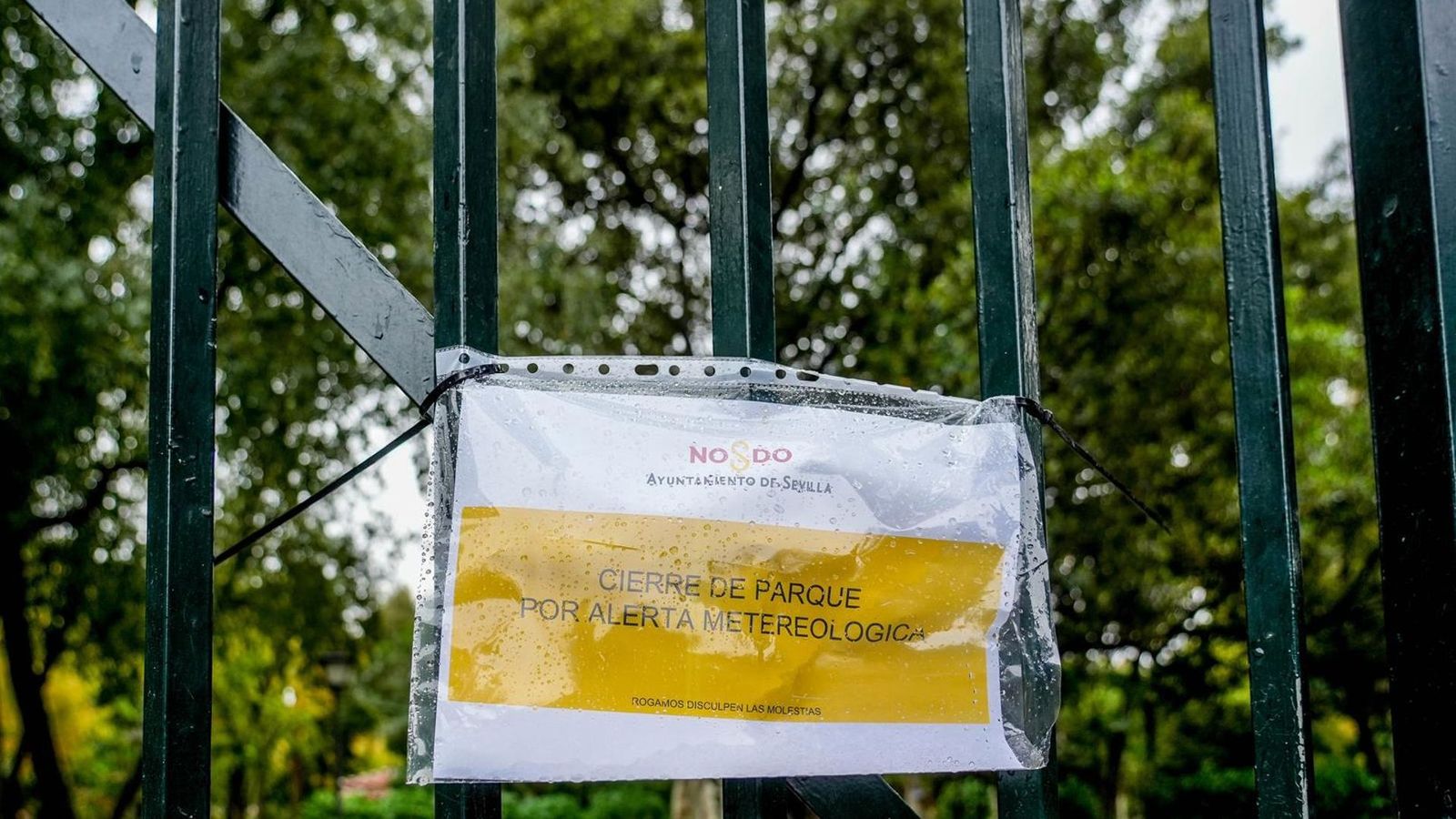 Cartel en una reja de entrada a un parque de Sevilla que indica el cierre por alerta meteorológica