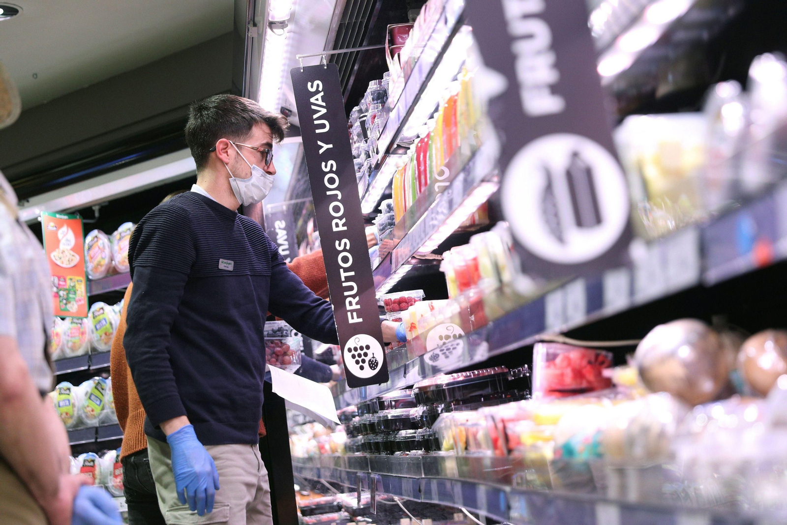 Un joven hacen la compra con mascarilla  y guantes en un supermercado.