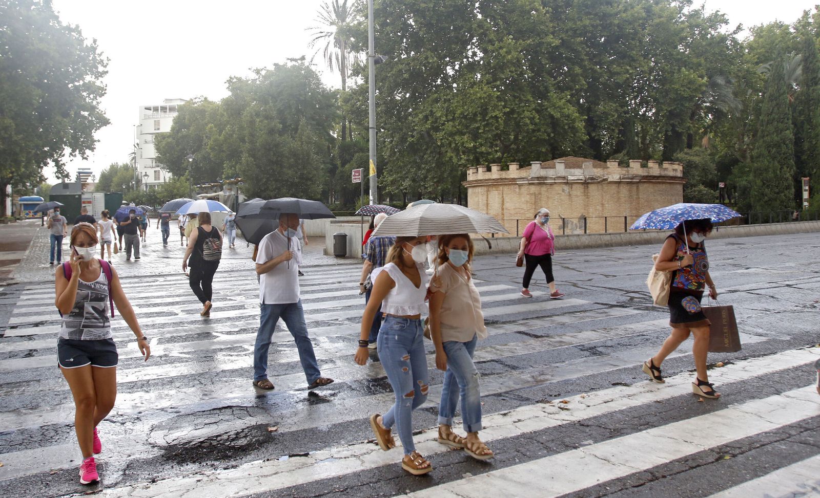 Gente con mascarilla y paraguas cruzan el paso de peatones del Paseo de la Victoria.