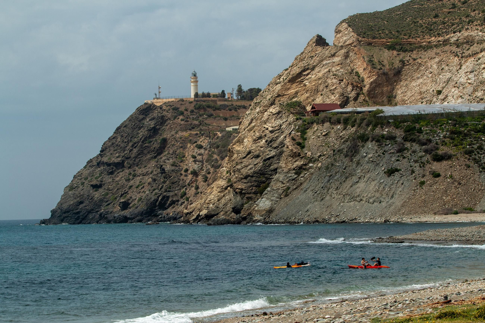Varias personas en Kayak por la playa de La Chucha con el faro Sacratif de fondo.